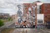 Grote zwart-wit muurschildering op een bakstenen gebouw met surrealistische figuren, schedels en abstracte structuren