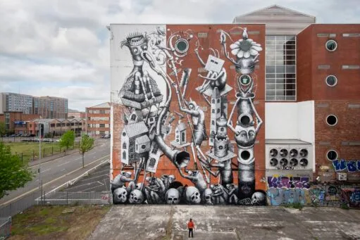 Grote zwart-wit muurschildering op een bakstenen gebouw met surrealistische figuren, schedels en abstracte structuren