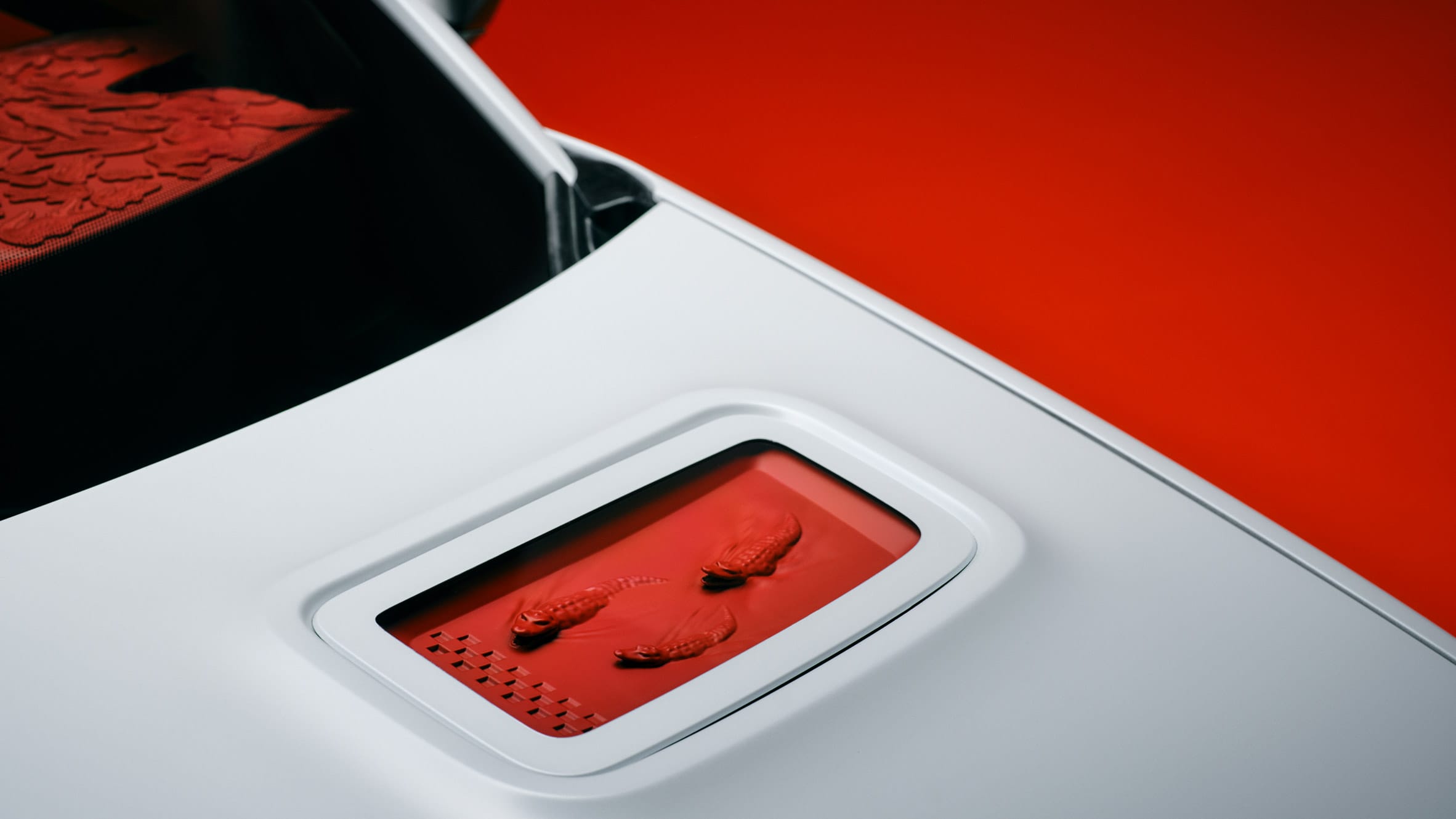 Close-up van een witte motorkap met een rood paneel waarin drie kleine krokodillen zijn verwerkt