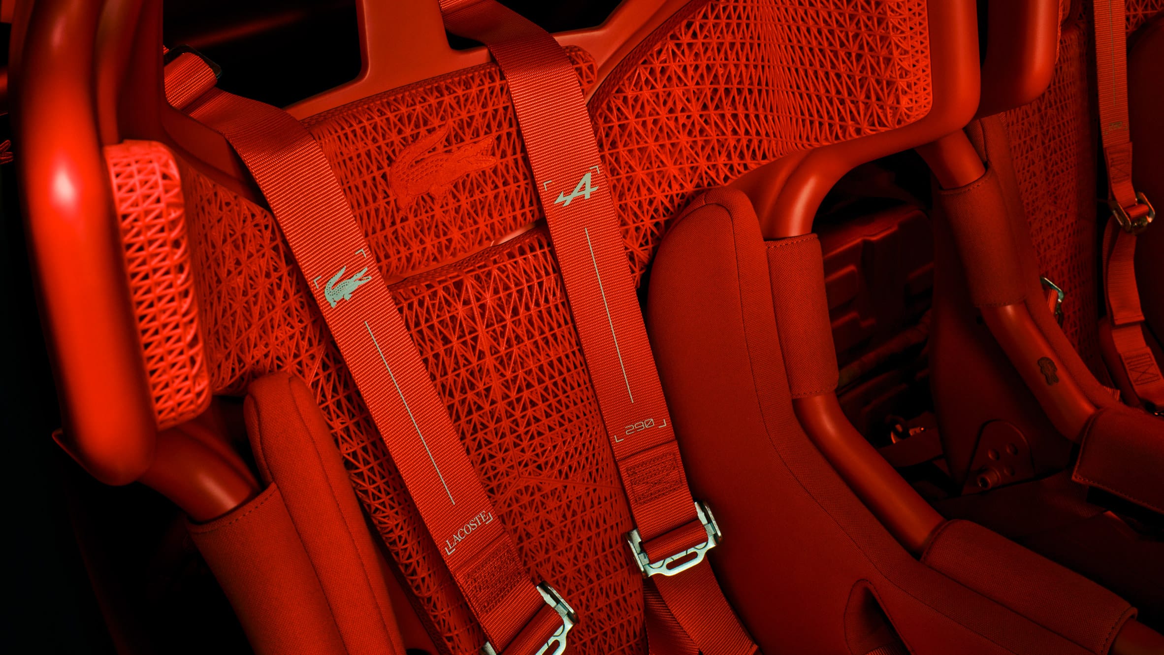 Detail van een rode Alpine A290 sportstoel met 3D-geprint gaaswerk, Lacoste-logo en vierpuntsgordels