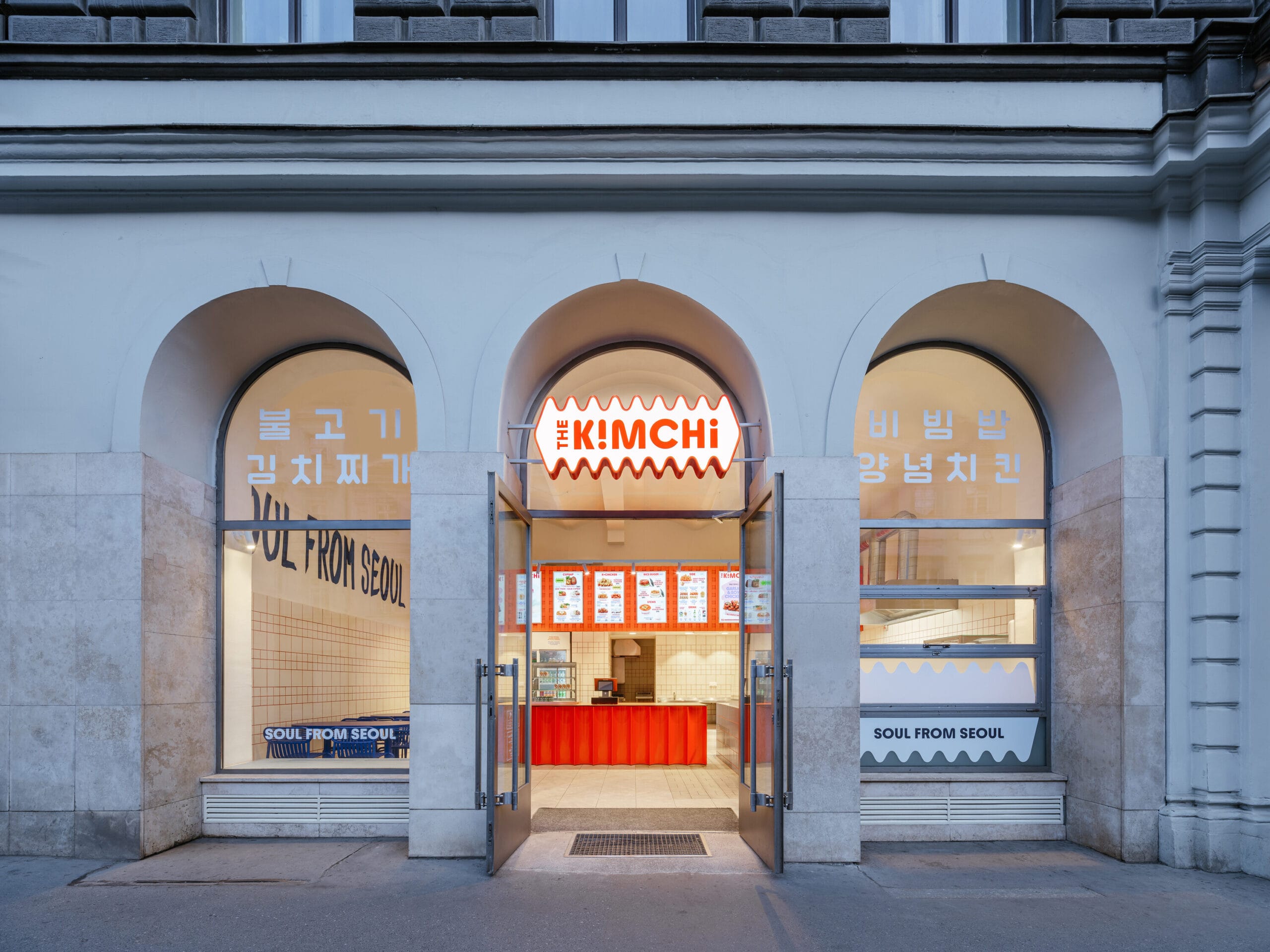 Voorgevel van Koreaans restaurant The Kimchi in Praag met drie bogen, een verlicht logo boven de ingang en een modern interieur