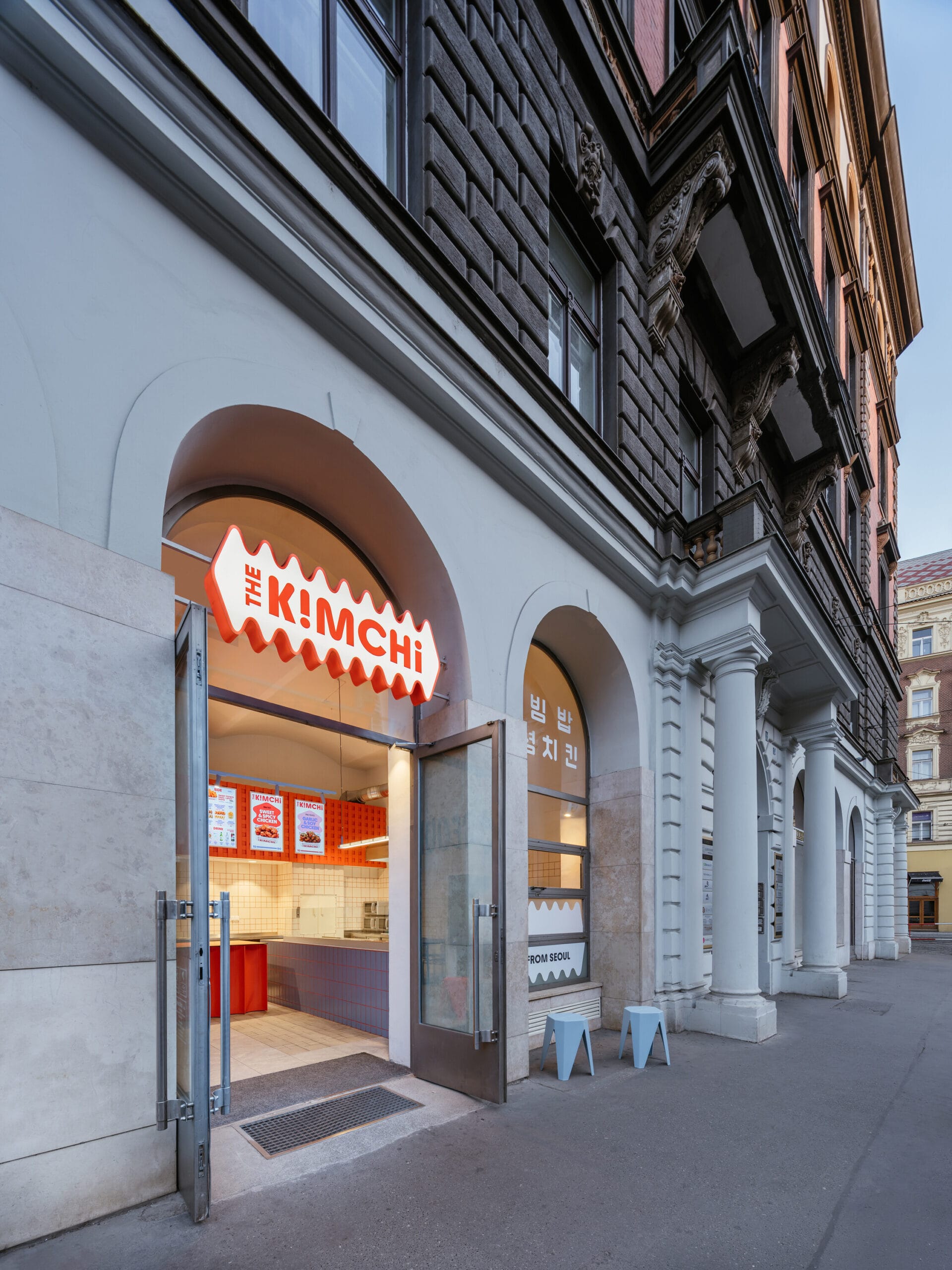 De voorgevel van restaurant The Kimchi in Praag met een opvallend oranje uithangbord boven de openstaande glazen deuren