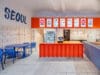 Modern interieur van het Koreaans restaurant The Kimchi in Praag, met een feloranje balie, blauwe tafels en stoelen, en menuborden aan de muur