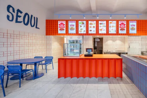 Modern interieur van het Koreaans restaurant The Kimchi in Praag, met een feloranje balie, blauwe tafels en stoelen, en menuborden aan de muur