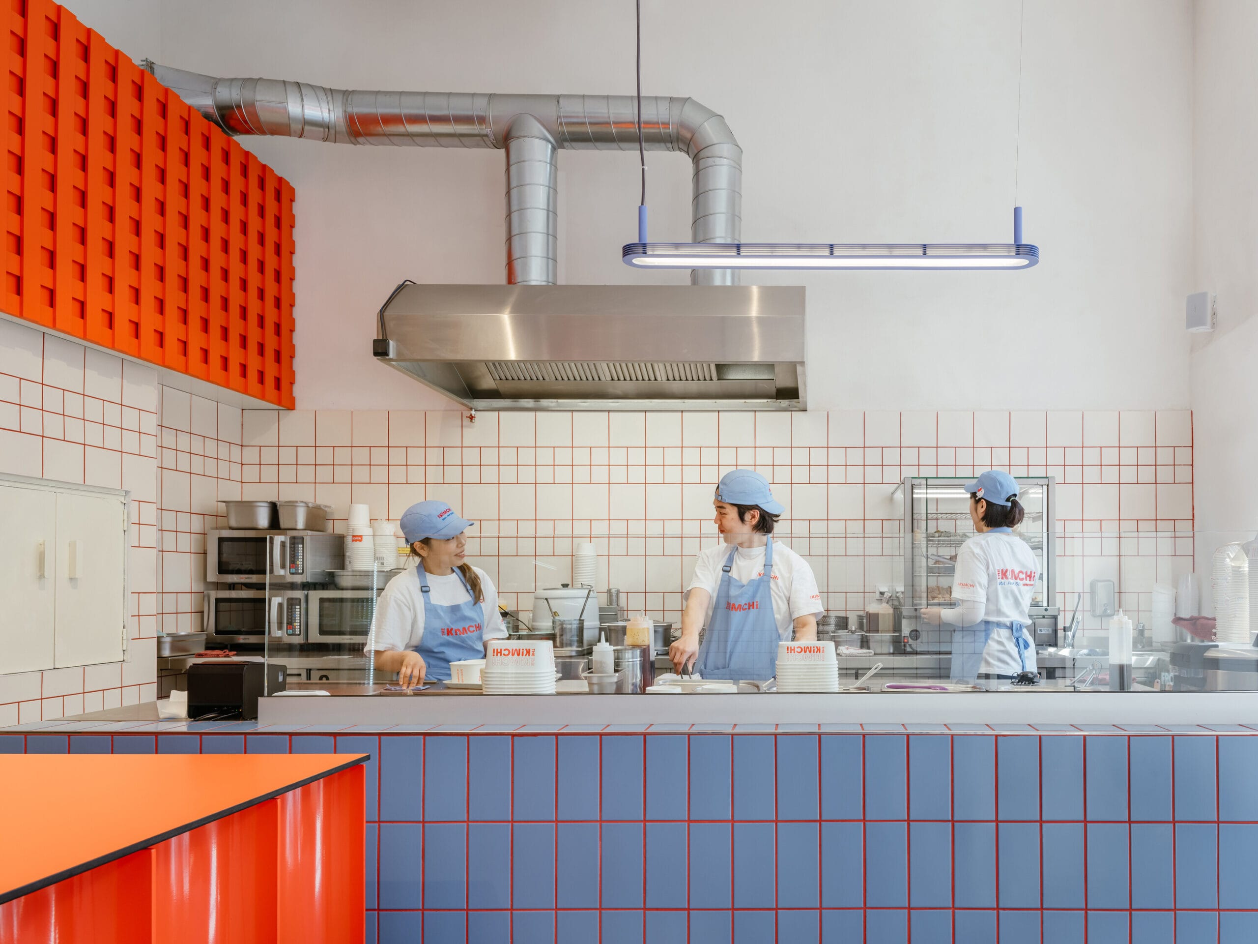 Drie medewerkers in blauwe schorten en petten aan het werk in de modern ingerichte keuken van restaurant The Kimchi in Praag