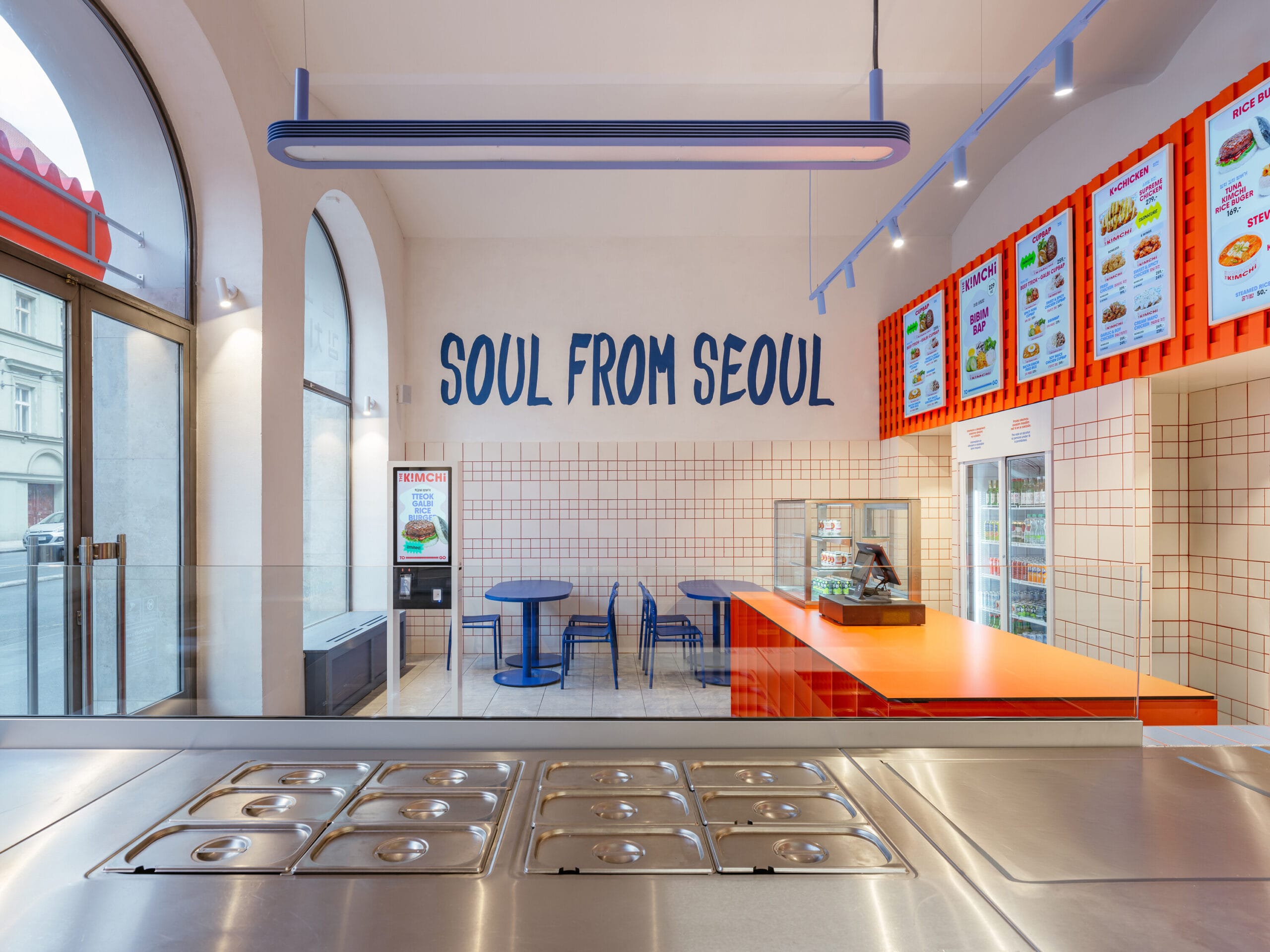 Modern interieur van het Koreaans restaurant The Kimchi in Praag met de tekst Soul from Seoul op de muur, blauwe tafels en een oranje balie