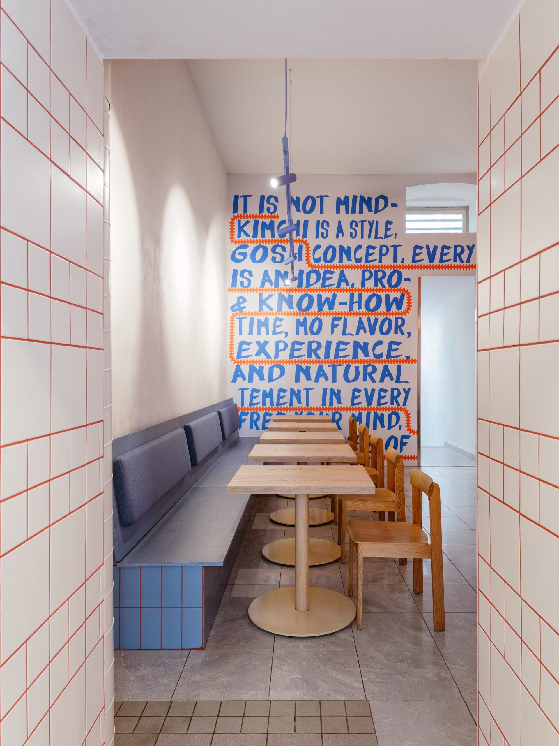 Modern interieur van restaurant The Kimchi in Praag, met houten tafels, een blauwe bank en een muur met grote blauwe tekst