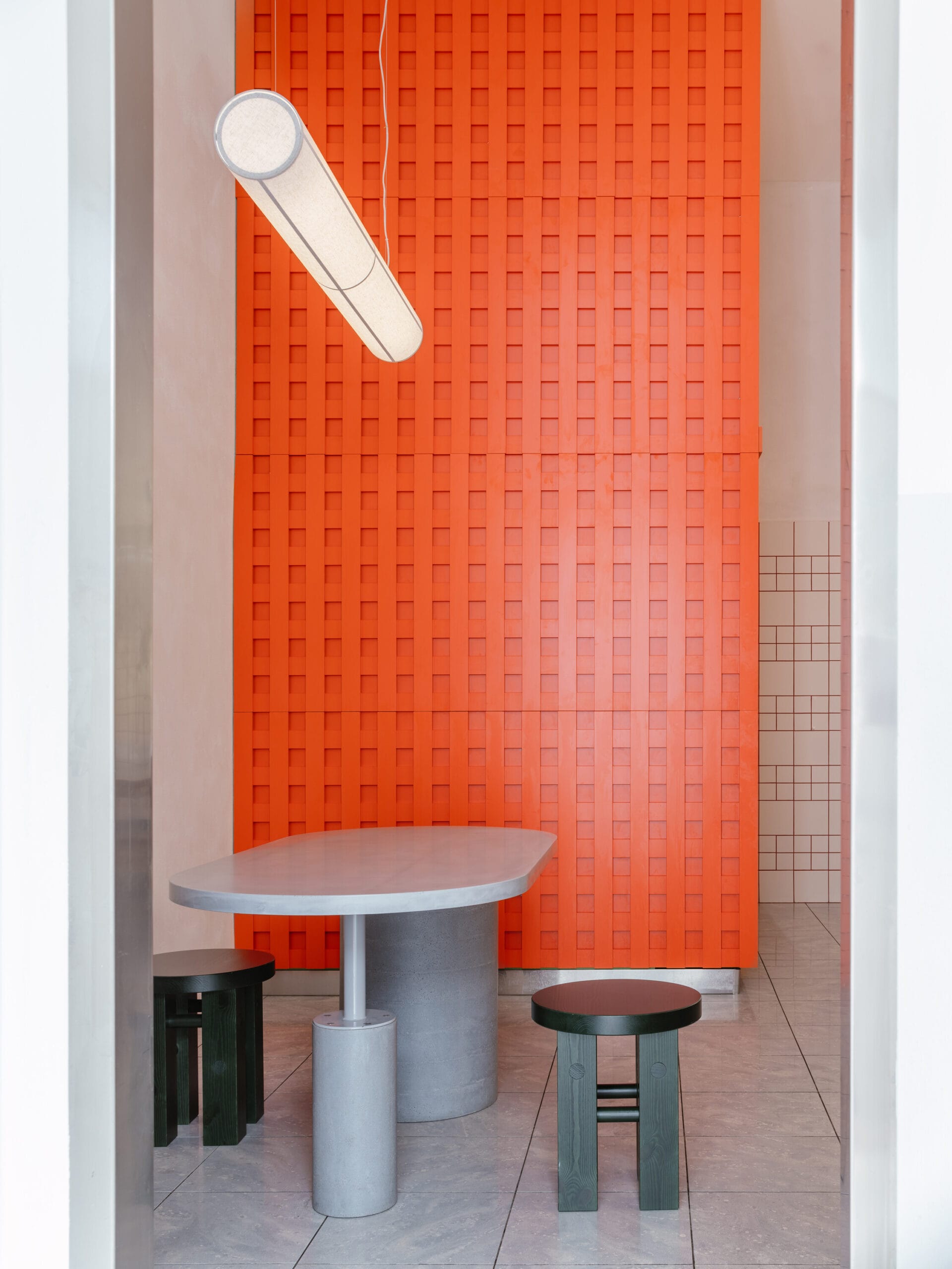 Modern interieur van restaurant The Kimchi in Praag, met een grijze tafel, zwarte krukjes en een opvallende oranje wand met een rasterpatroon