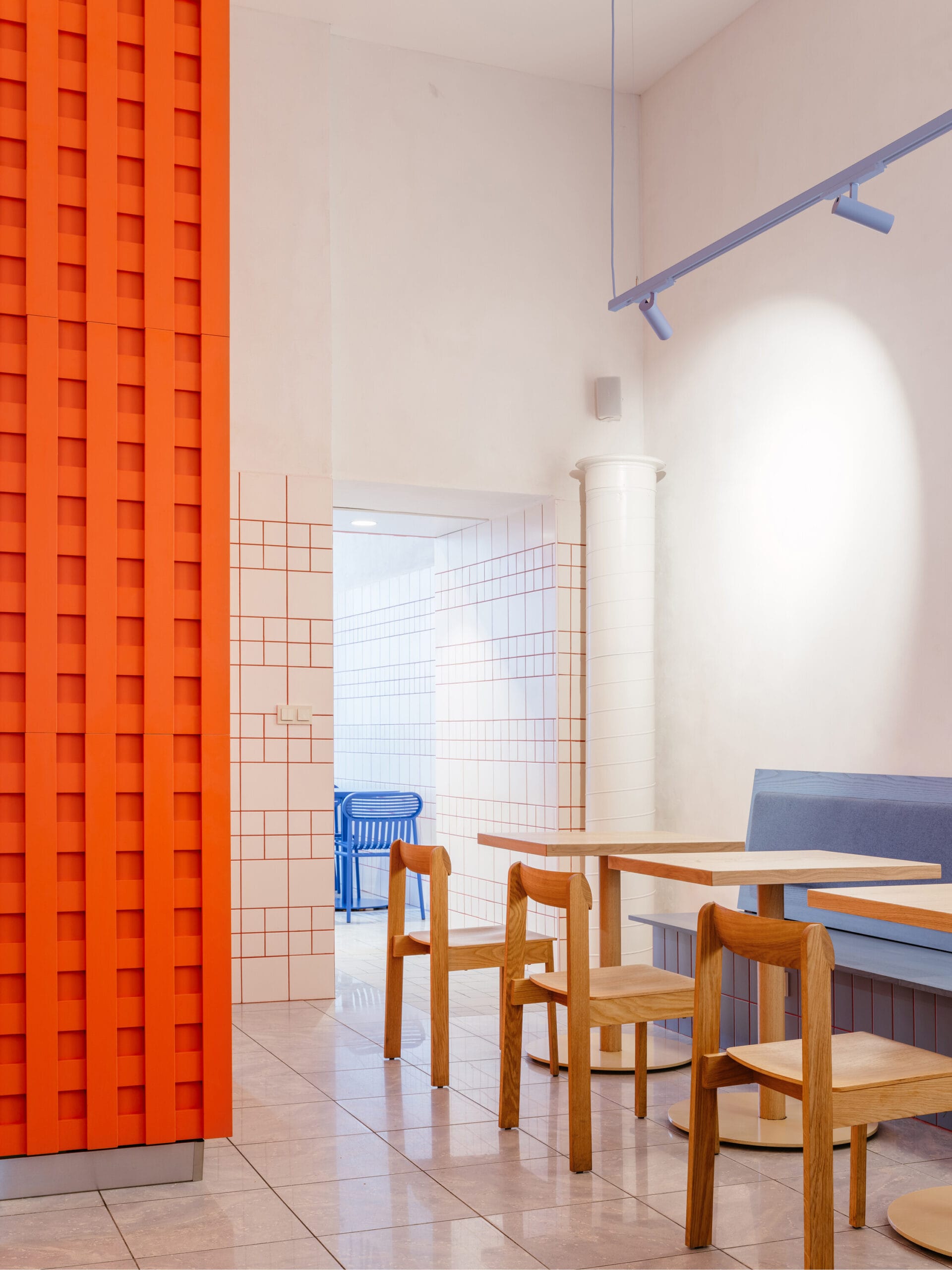 Modern interieur van The Kimchi in Praag, met houten tafels en stoelen, een opvallende oranje wand en witte betegelde muren