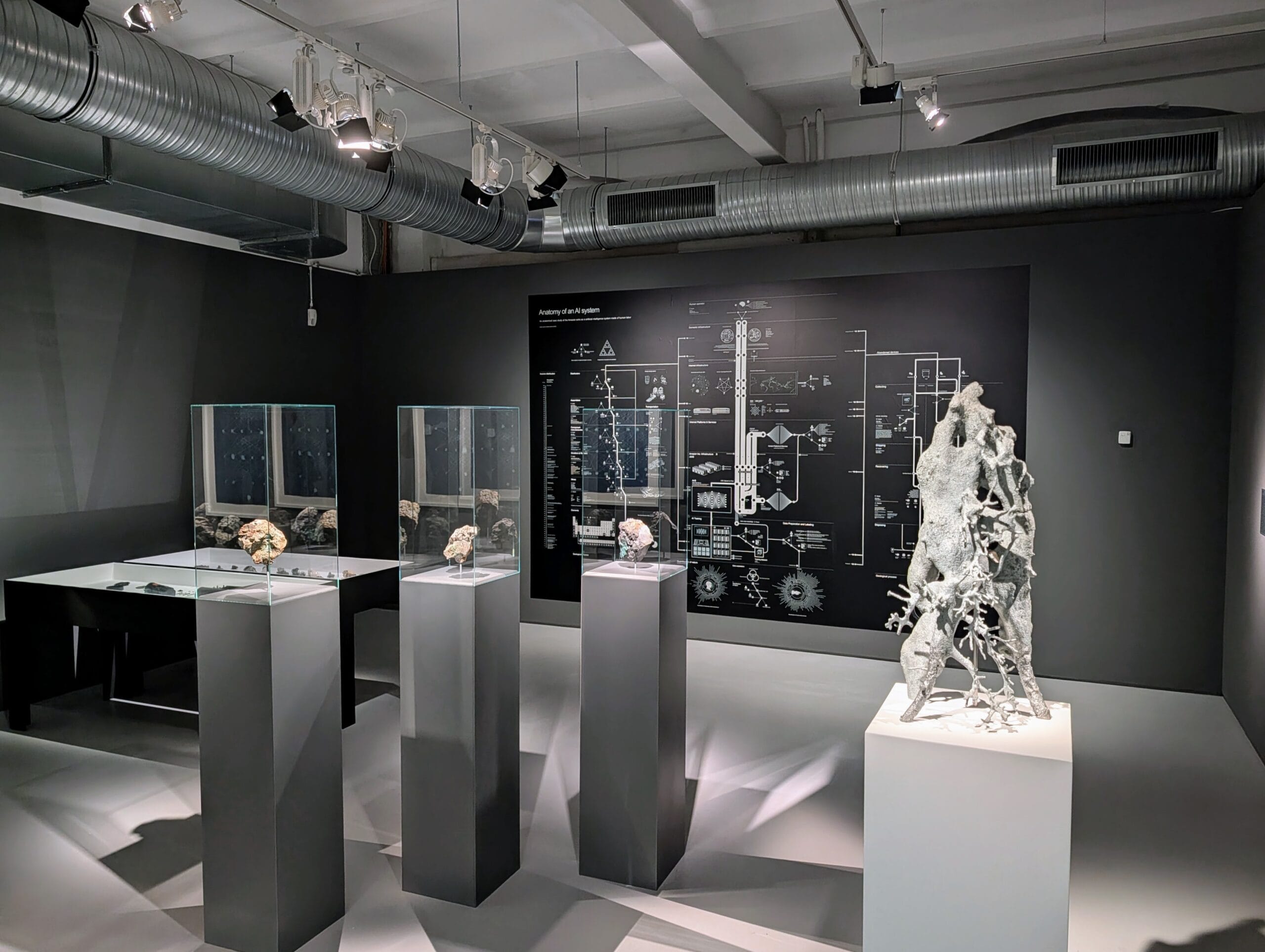 Expositie over AI in museum Schirn met sculpturen op sokkels en een grote wandkaart getiteld Anatomy of an AI system