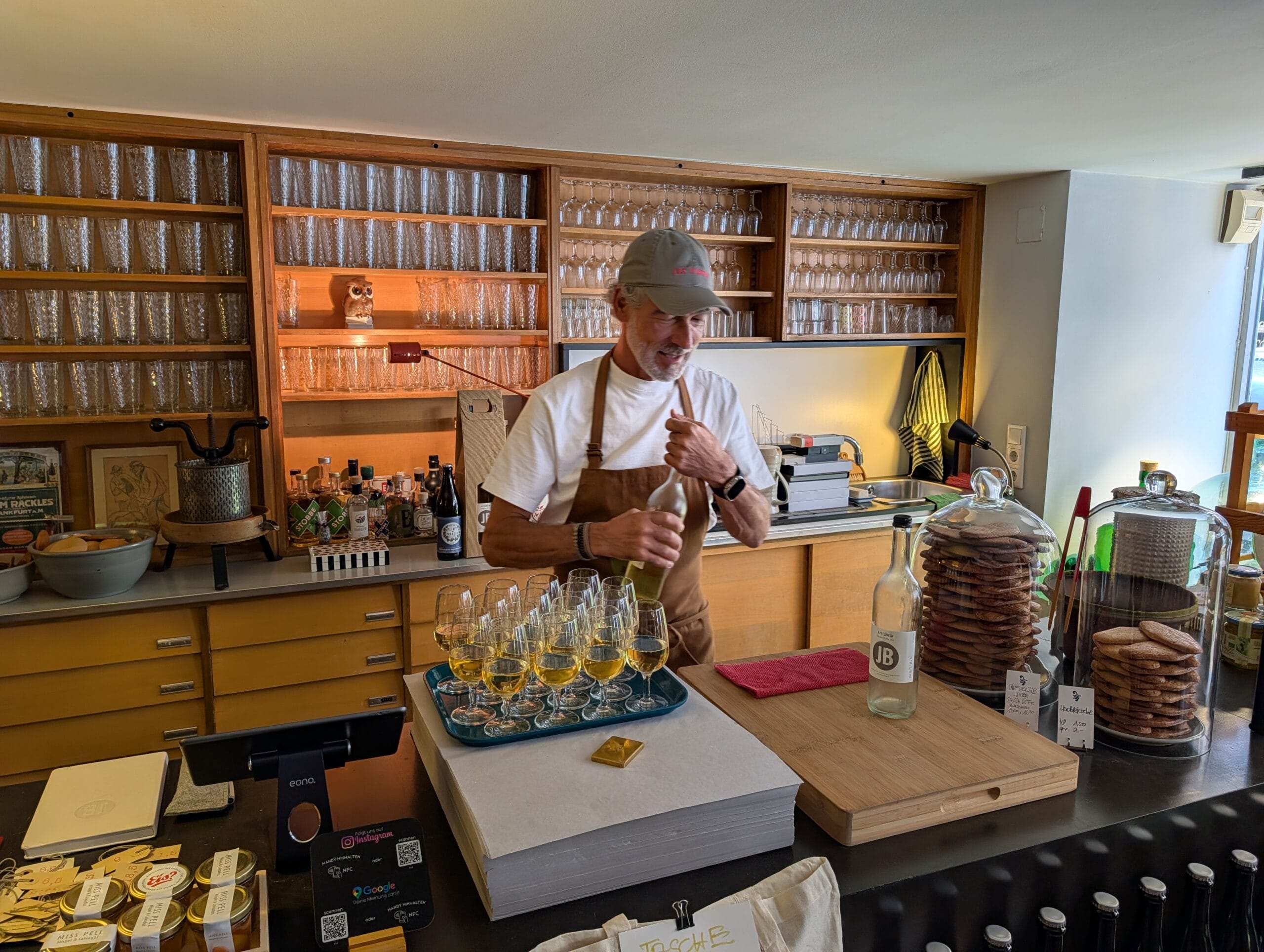 Jens Becker opent een fles apfelwein achter de bar van zijn proeflokaal, met een dienblad vol gevulde glazen