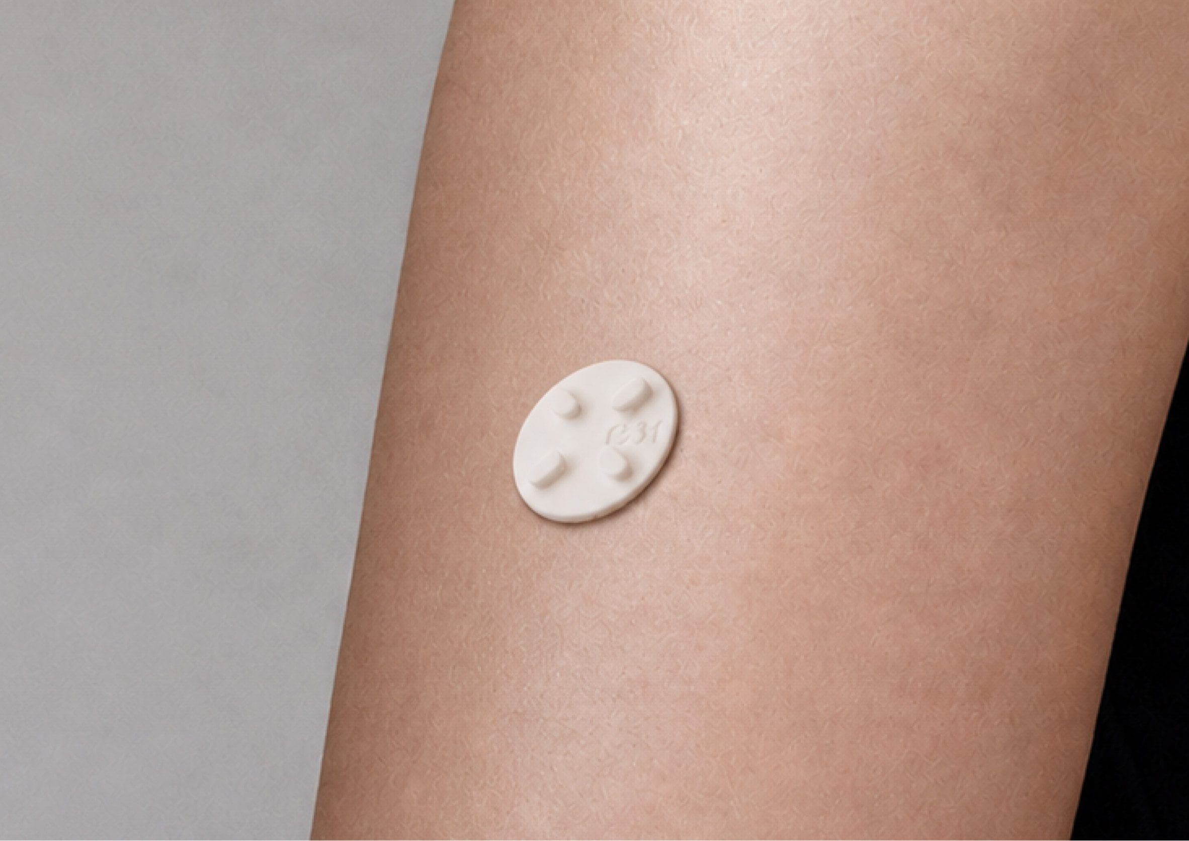 Een kleine, witte, ovale CipherX-patch met micronaalden aangebracht op de huid van een arm