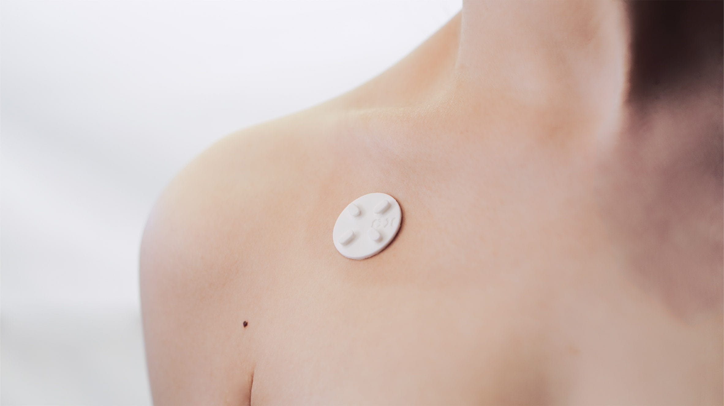 Een witte ronde CipherX-applicator met micronaalden aangebracht op de huid van een schouder