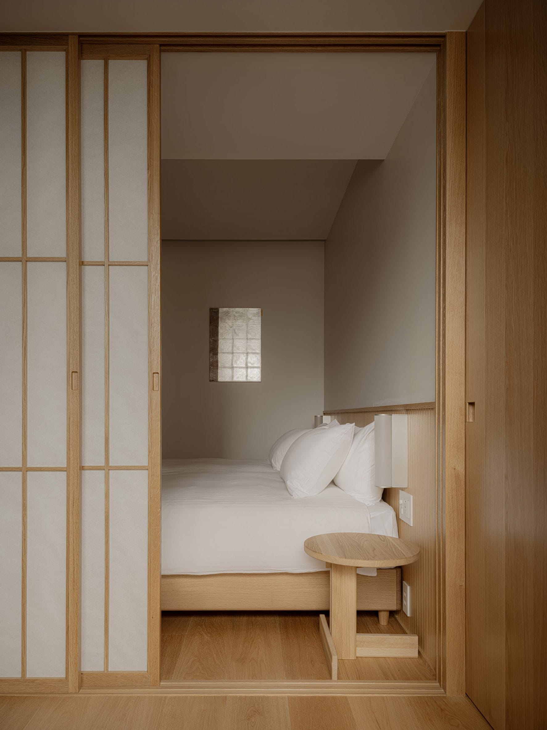 Minimalistische slaapkamer in Japanse stijl met houten schuifdeuren, een laag bed met wit beddengoed en een houten bijzettafel