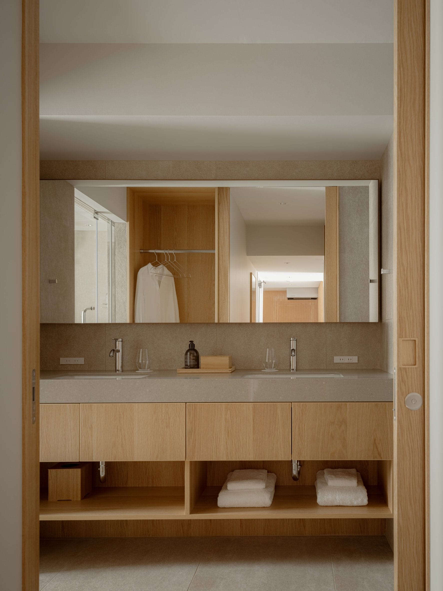 Moderne badkamer met een dubbele wastafel, houten meubel, grote spiegel en een open kast met witte handdoeken
