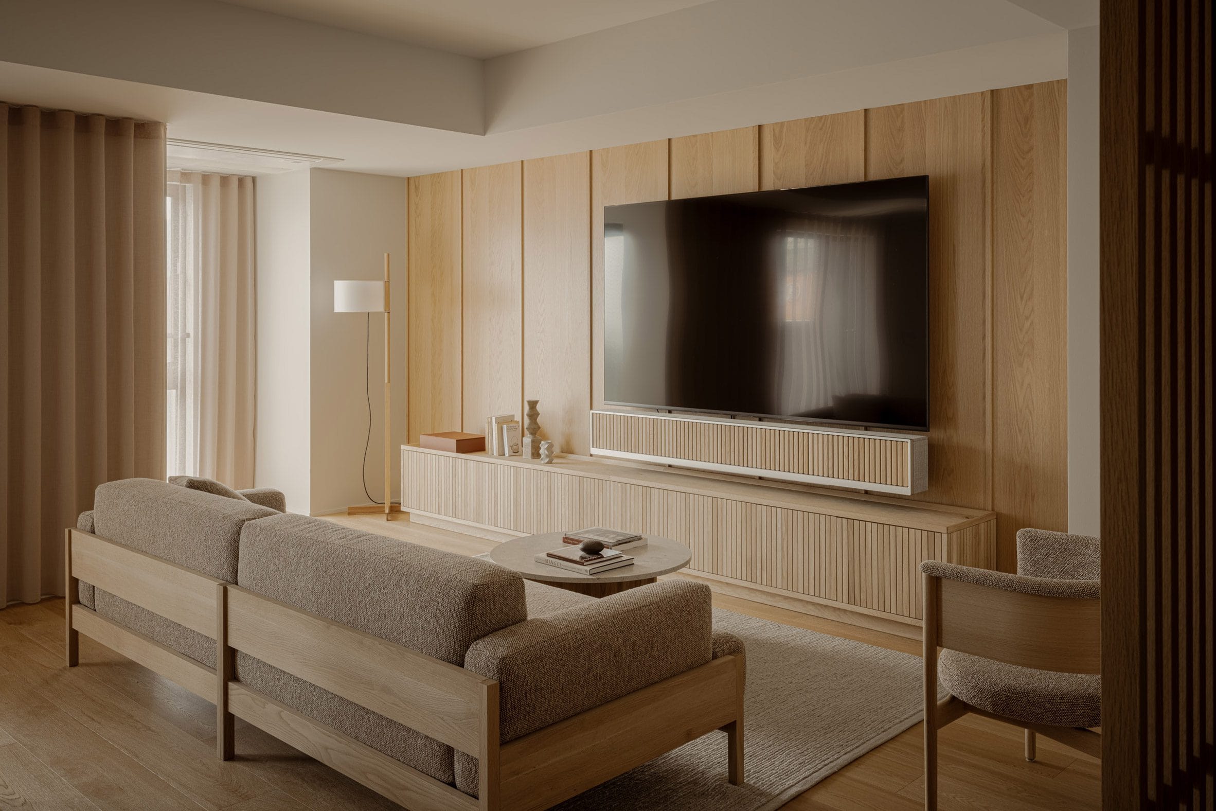 Modern interieur van een woonkamer met houten wandpanelen, een grote televisie en minimalistische meubels in beige tinten
