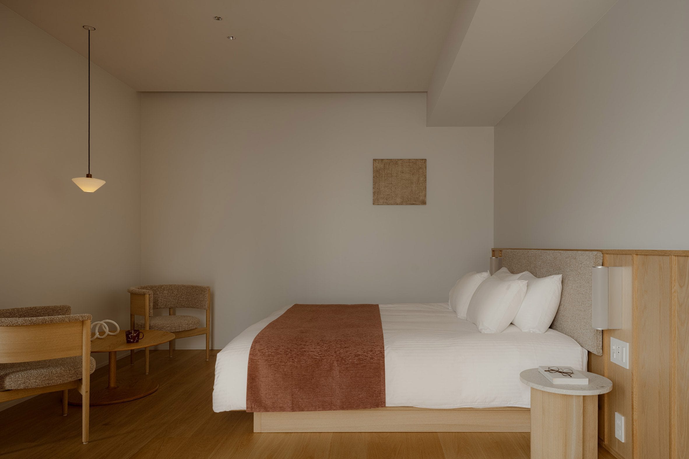 Minimalistische hotelkamer met een tweepersoonsbed, houten meubilair en een zithoek in neutrale aardetinten