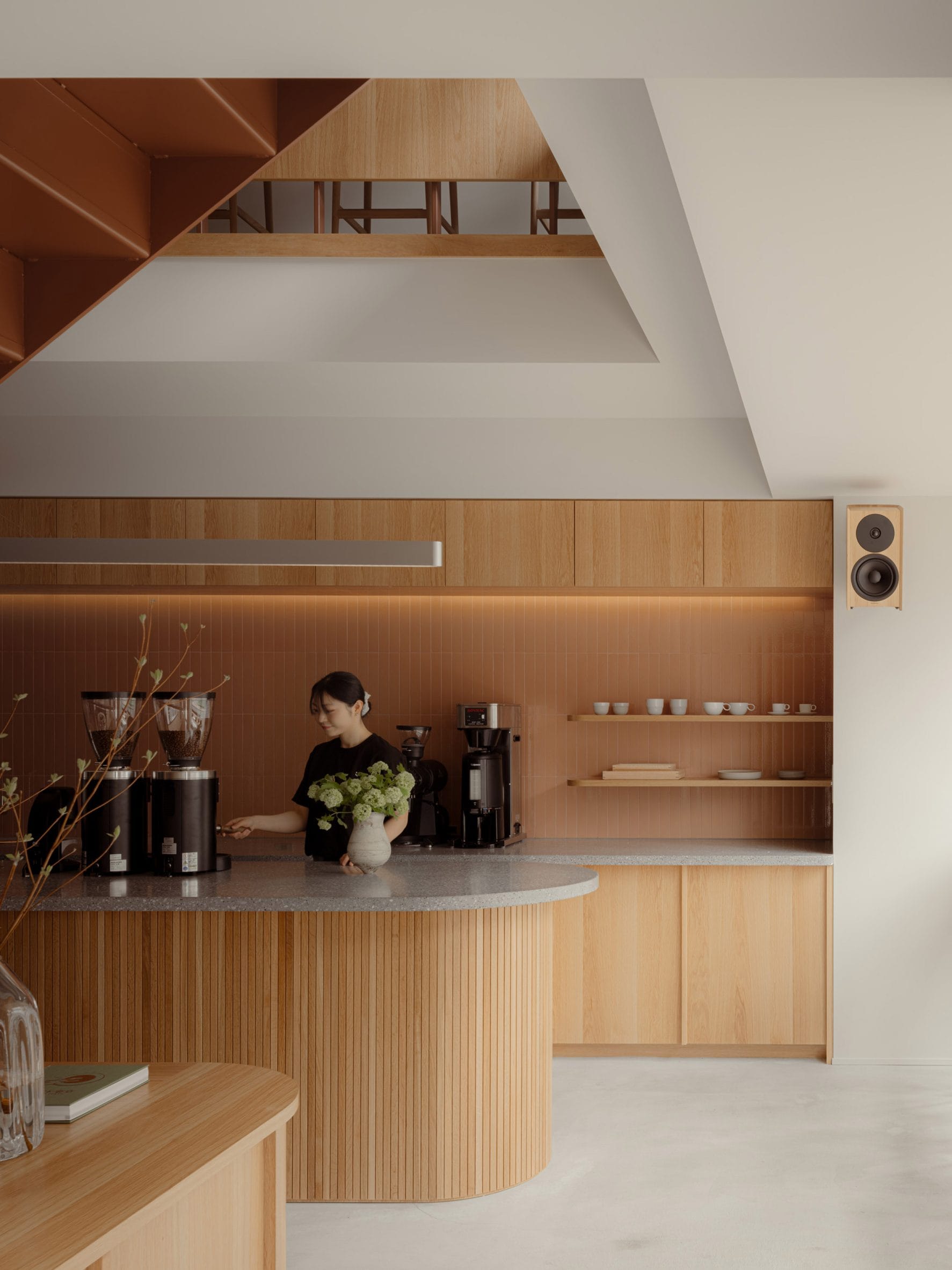 Een barista werkt achter een houten bar in een modern, minimalistisch café met warme aardetinten en houten accenten