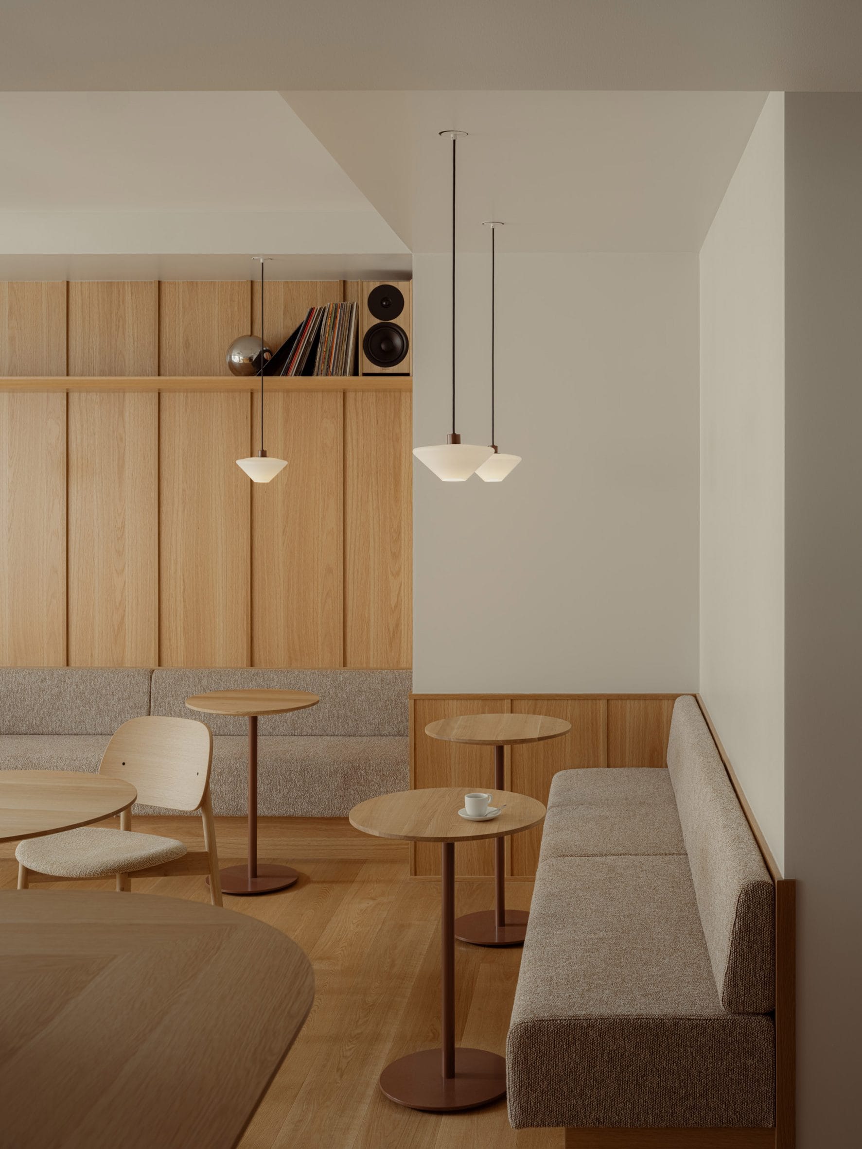 Modern interieur van een café met houten wandpanelen, ronde tafels en grijze gestoffeerde banken