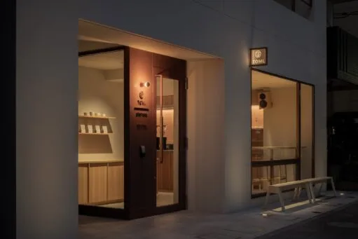 De minimalistische voorgevel van koffiebar TOMI bij avondlicht, met een glazen pui en houten interieur