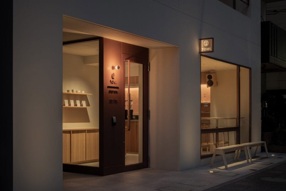 De minimalistische voorgevel van koffiebar TOMI bij avondlicht, met een glazen pui en houten interieur