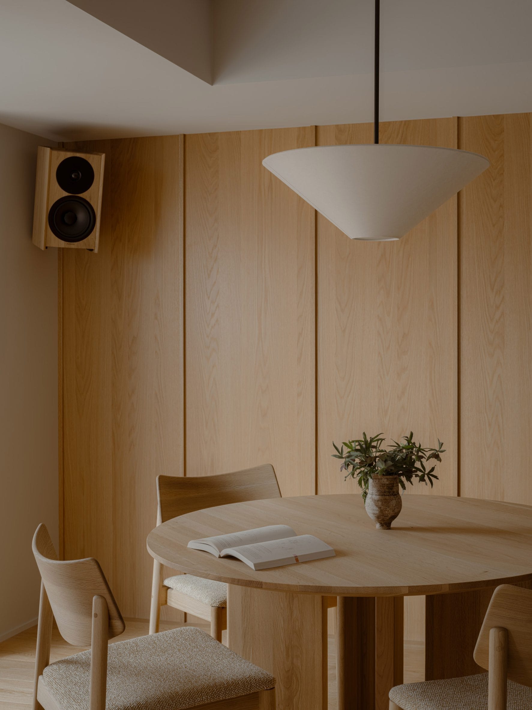 Minimalistisch interieur met een ronde houten eettafel, bijpassende stoelen en een houten wandpaneel