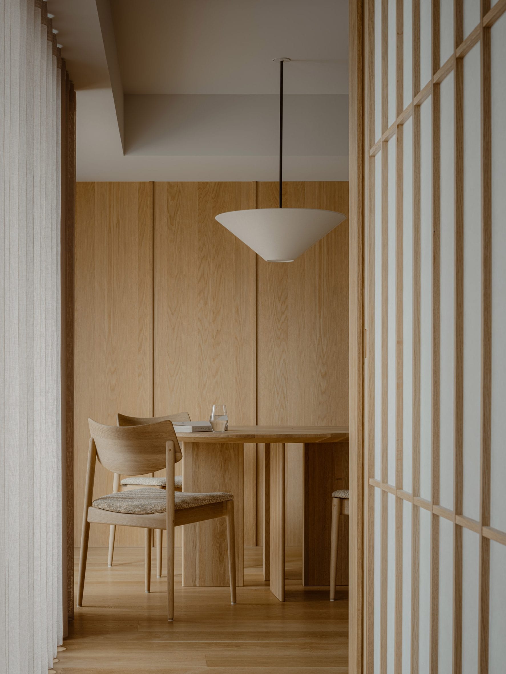 Minimalistisch interieur met een houten eettafel, stoelen en wandpanelen in Japanse stijl onder een kegelvormige hanglamp