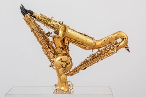 Een sculptuur van drie gouden saxofoons die in elkaar zijn gevlochten tot een abstracte, driehoekige vorm op een sokkel
