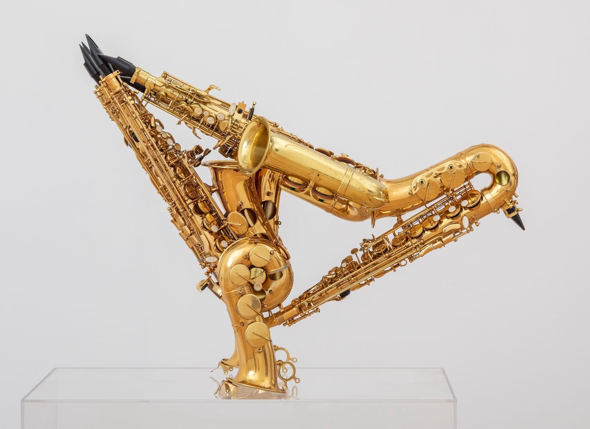 Een sculptuur van drie gouden saxofoons die in elkaar zijn gevlochten tot een abstracte, driehoekige vorm op een sokkel