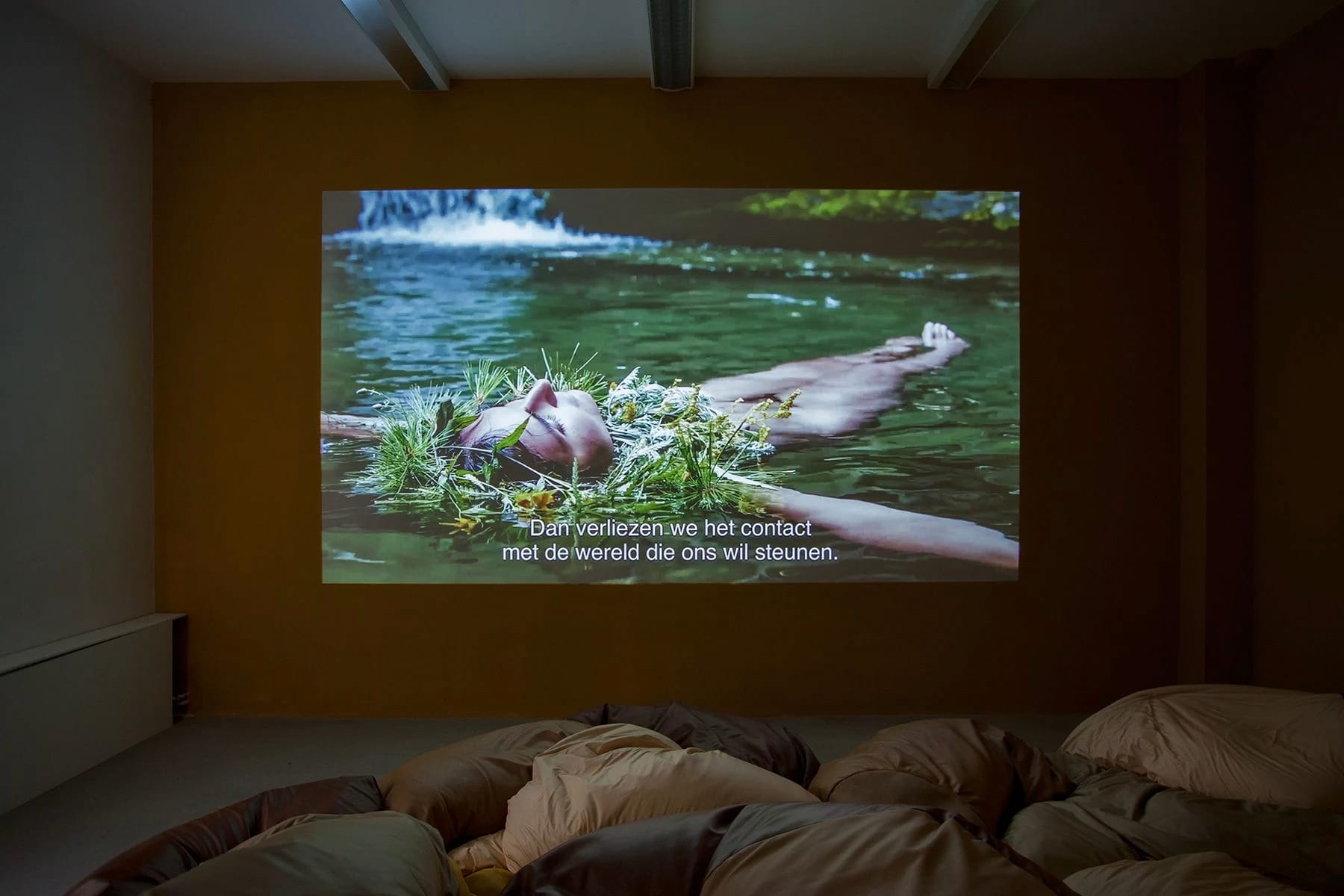 Zaaloverzicht van de video-installatie Night Soil #3, met een projectie van een persoon die in het water drijft