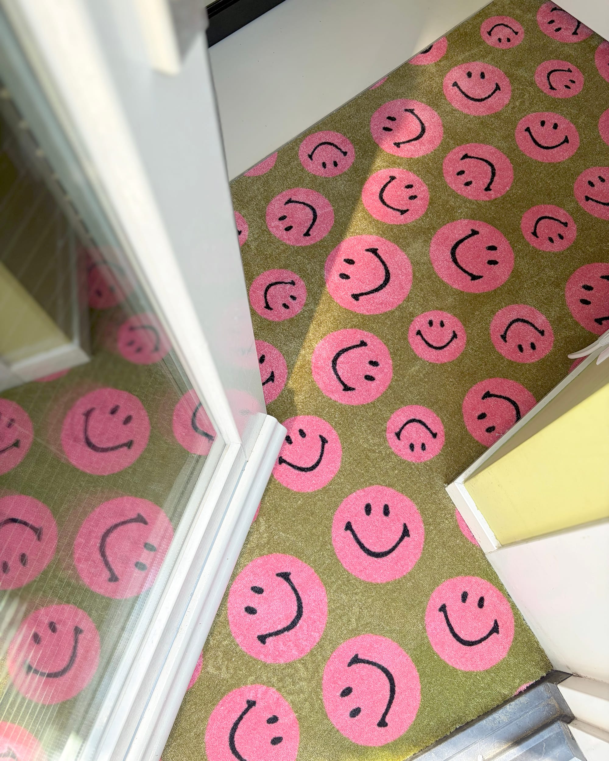 Op maat gemaakte deurmat in een gang met een patroon van roze smileys op een olijfgroene achtergrond