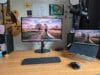 Werkplek met een houten bureau, AOC-monitor, laptop op een standaard, draadloos toetsenbord, muis en een microfoon