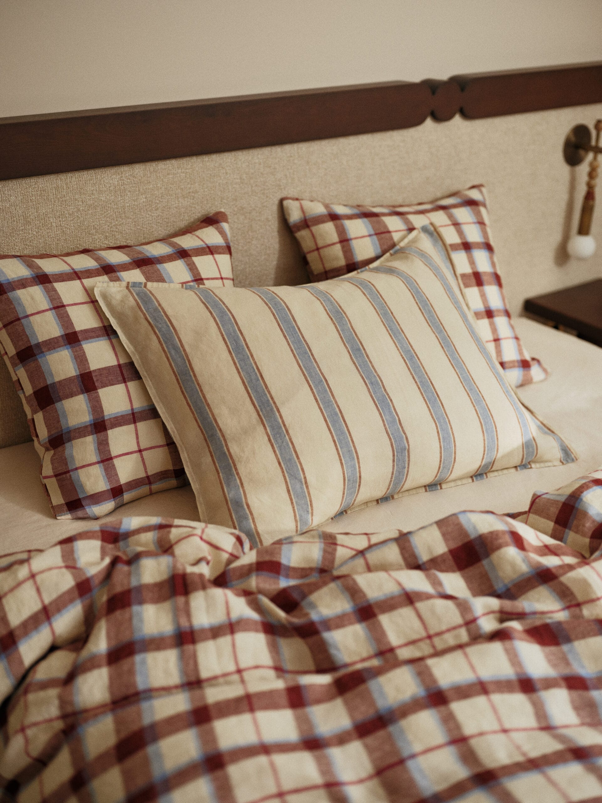 Bed met kussens en een dekbedovertrek in een rood-blauw ruitpatroon en een gestreept kussen, uit de Essentials collectie van Bonsoirs
