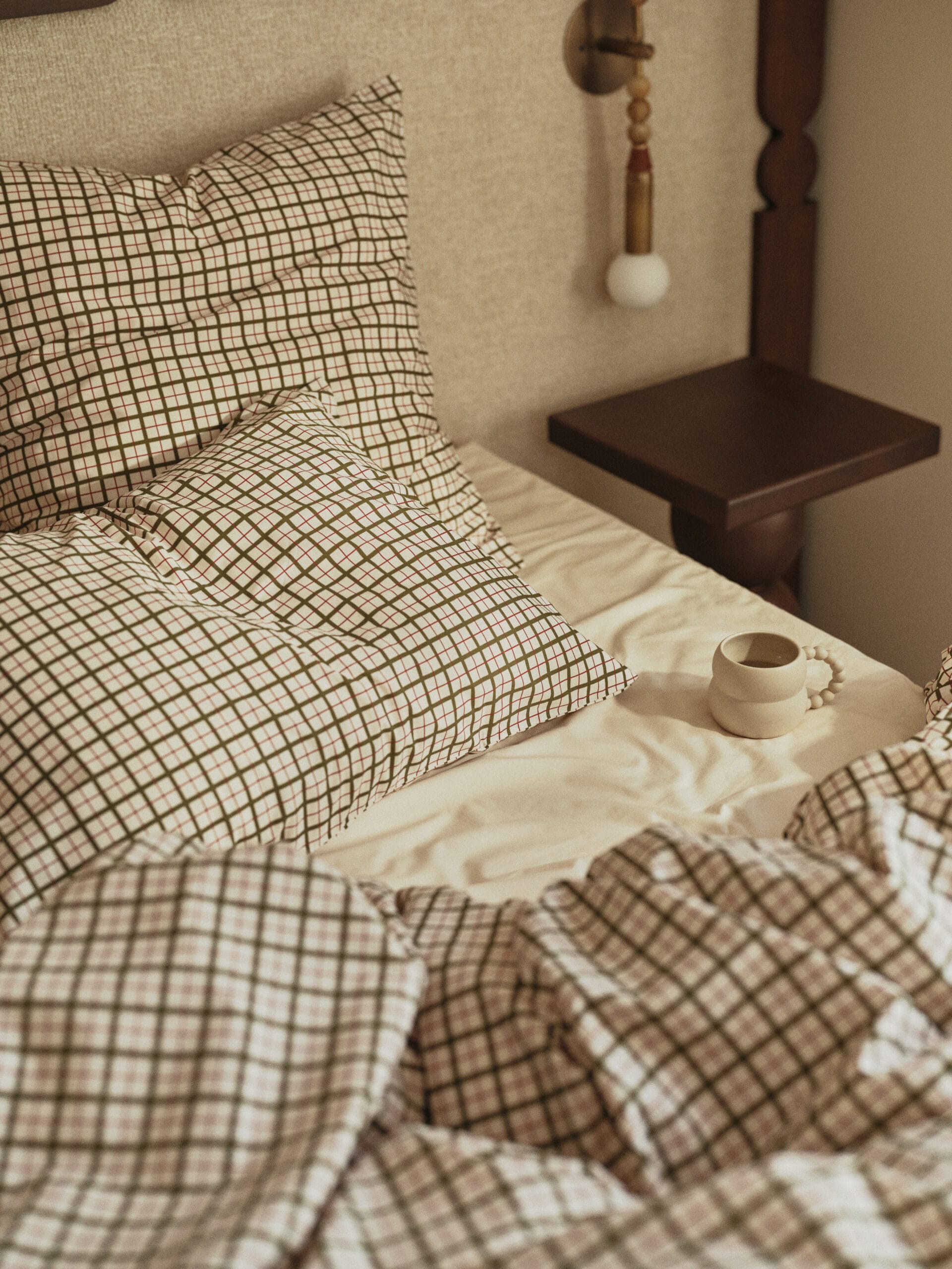 Opgemaakt bed met geruit beddengoed in groen en rood, met een beige mok op het laken naast de kussens, uit de Essentials collectie van Bonsoirs