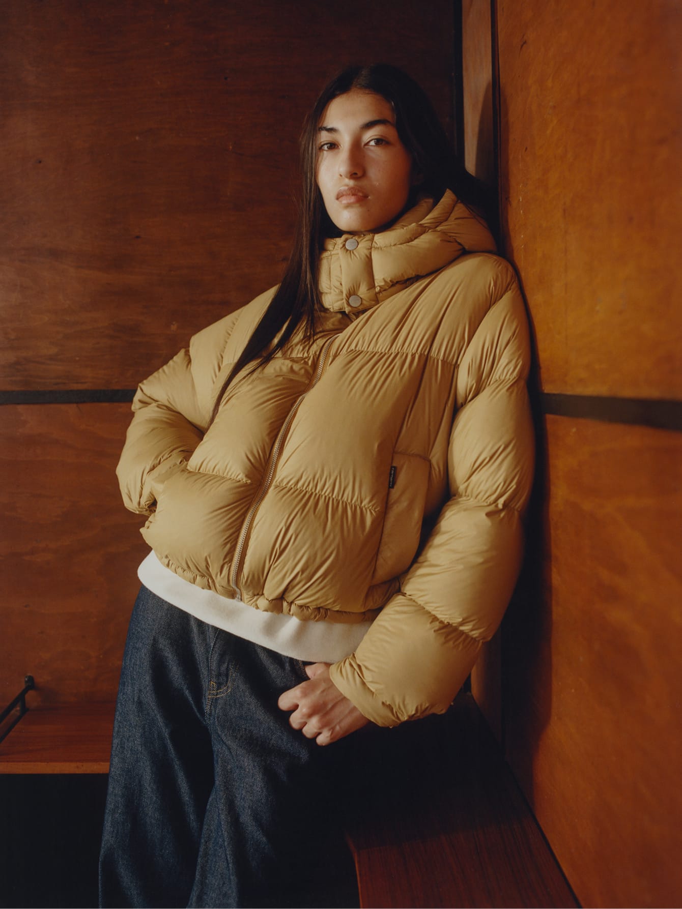 Model draagt een okergele gewatteerde winterjas en een donkere denim broek uit de Carhartt WIP Herfst/Winter collectie