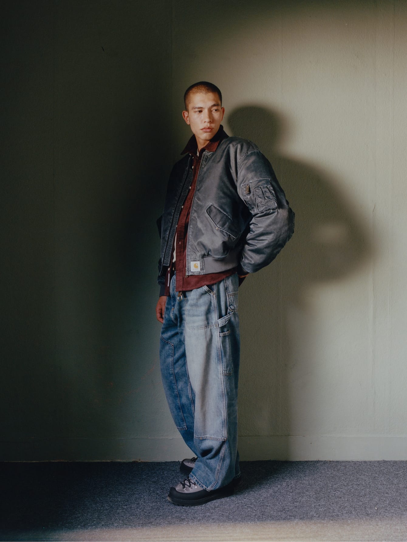 Model draagt een gewassen Orman Bomber-jack over een bordeauxrood overhemd en een ruimvallende denim Double Knee Pant