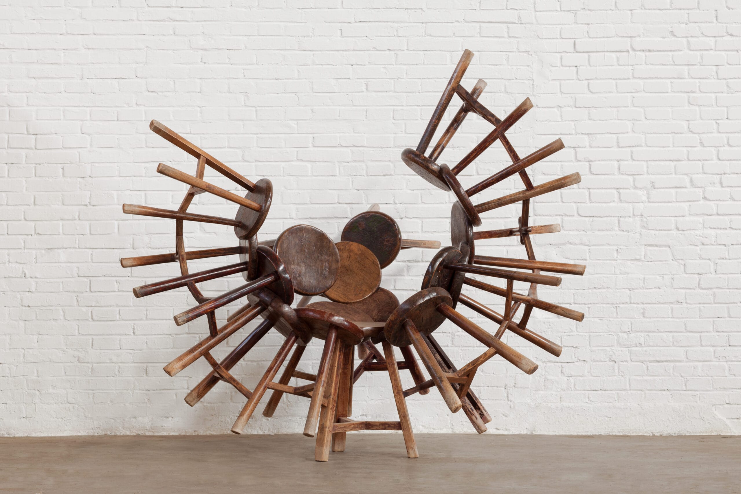 Sculptuur van in elkaar grijpende antieke houten krukken die samen een boogvormige structuur vormen, het gaat om het werk Grapes 2007-2015 18 wooden Qing Dynasty stools van Ai Weiwei