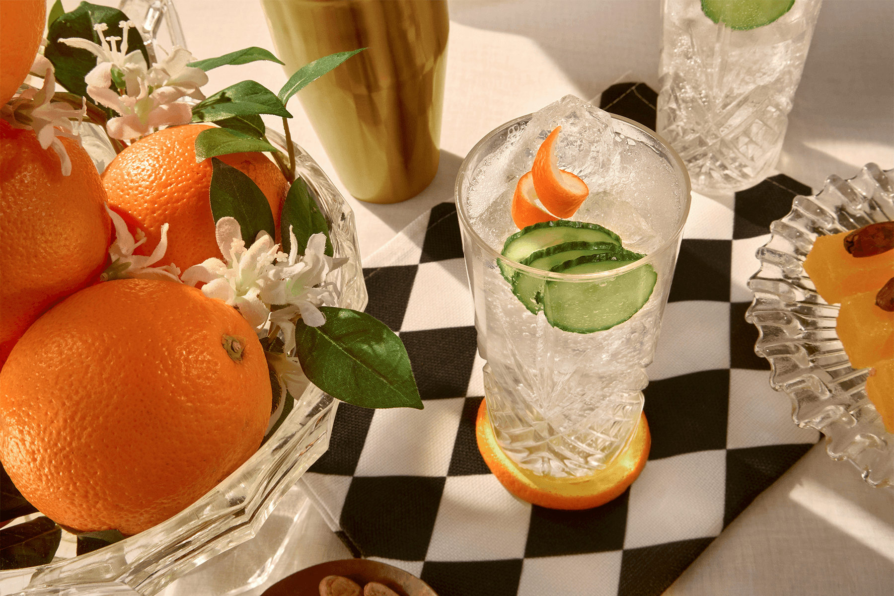 Een glas Another Hendrick’s Gin Tonic gegarneerd met komkommer en sinaasappelschil, naast een schaal met sinaasappels