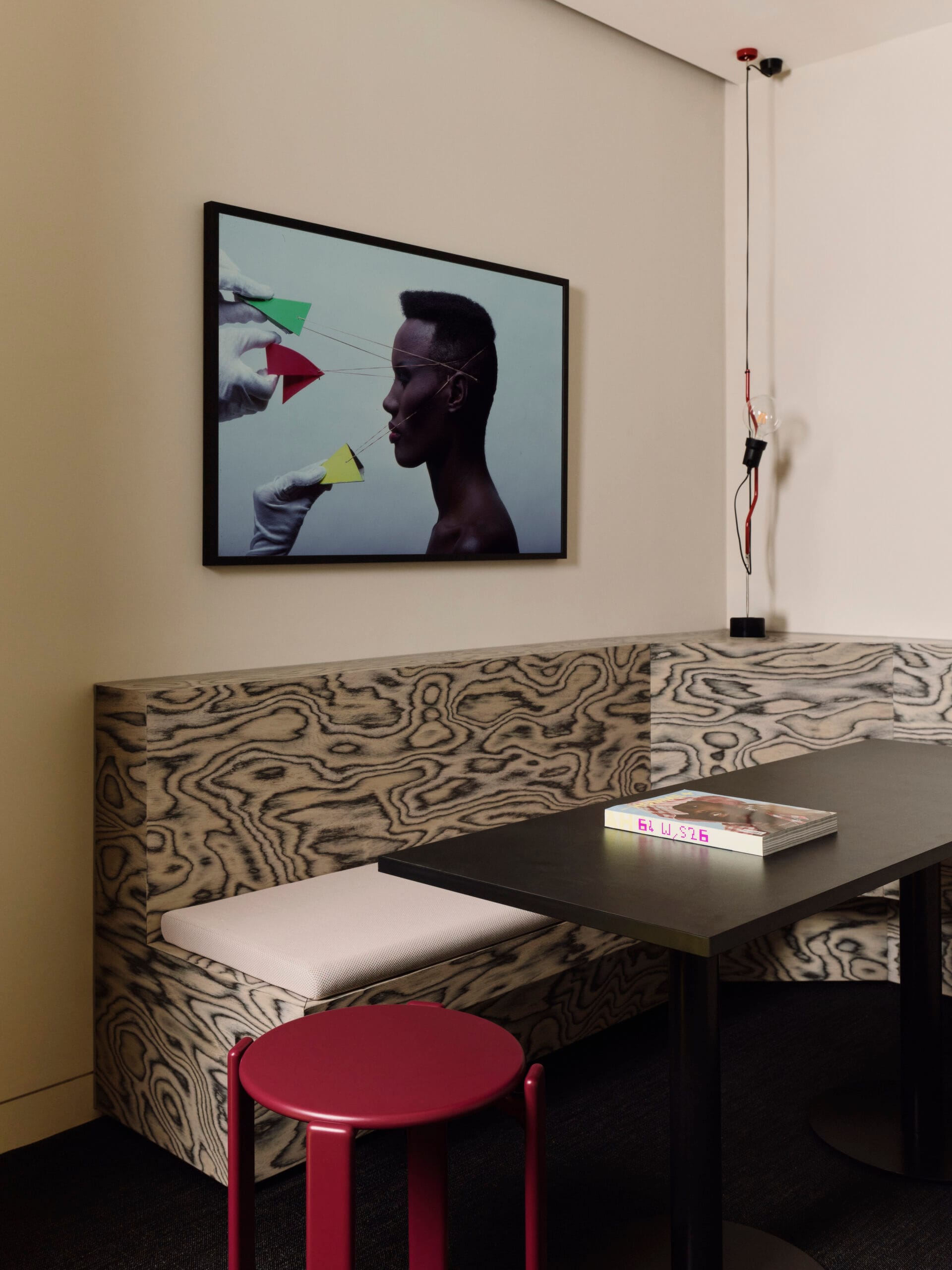 Een zithoek in het kantoor met een houten bank met opvallende nerf, een zwarte tafel en een portret van Grace Jones