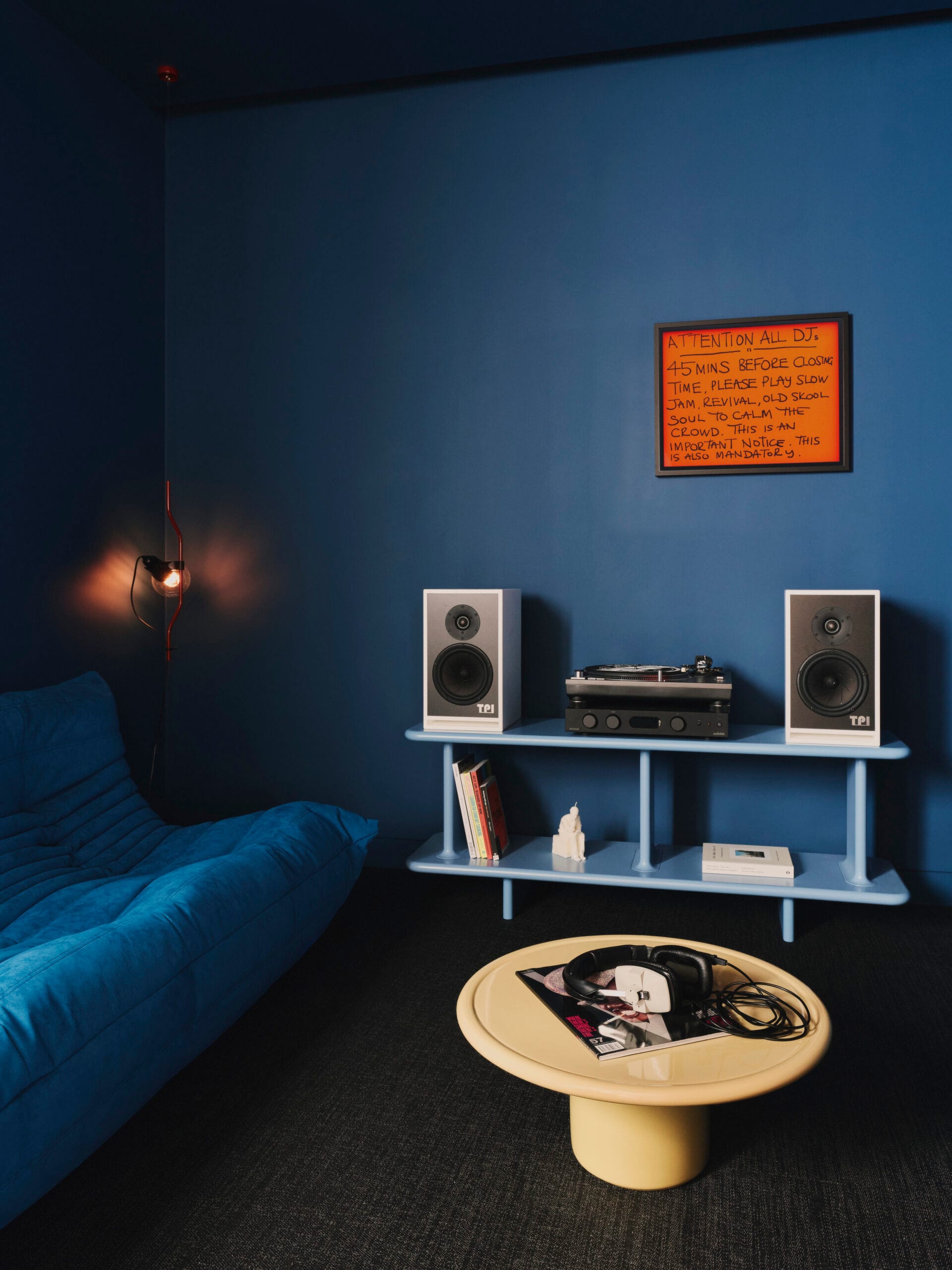 Blauwe luisterruimte met TPI-speakers, een platenspeler en een ingelijst kunstwerk van Jeremy Deller aan de muur