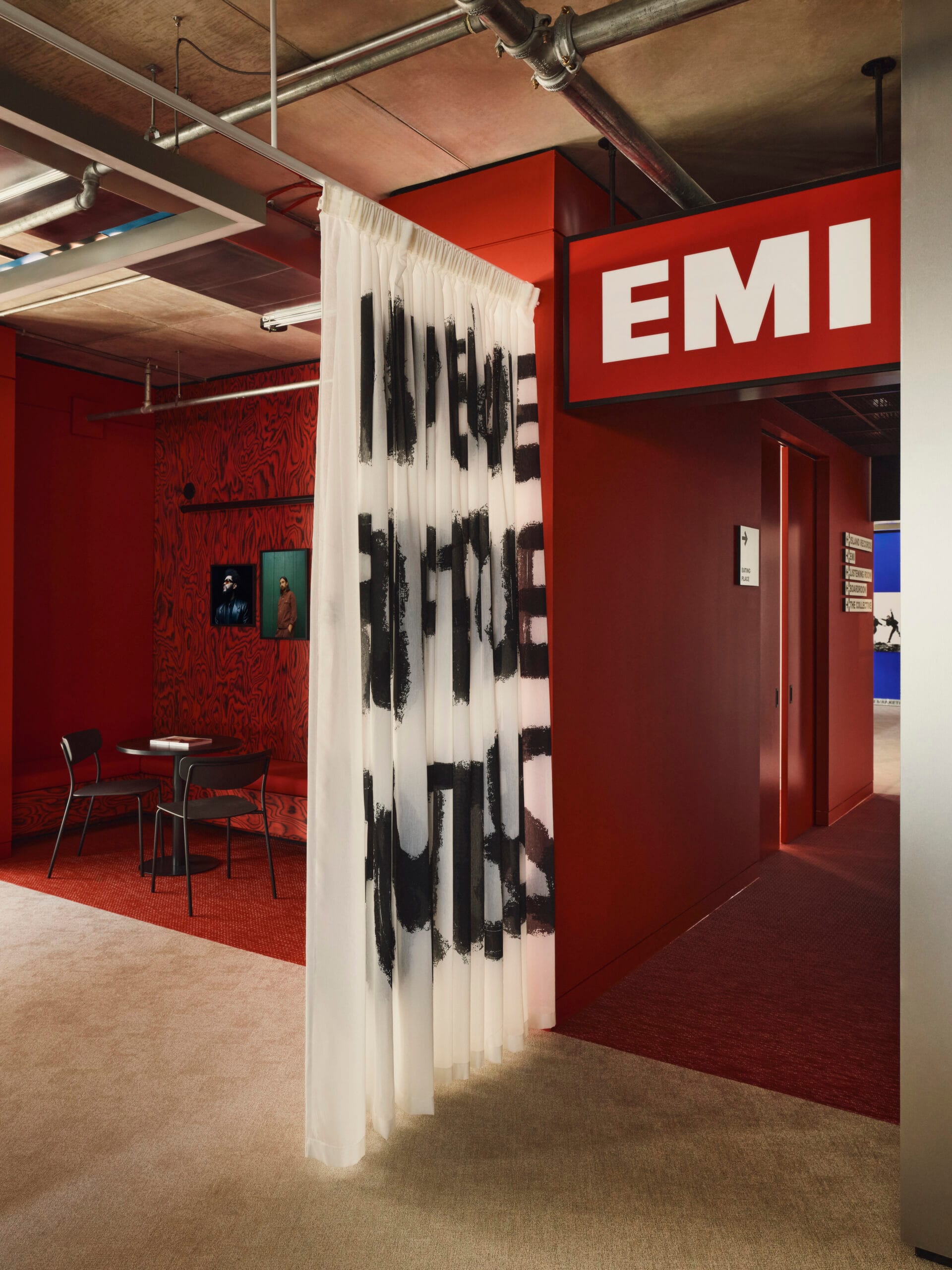 Interieur van het EMI-kantoor met rode wanden, een groot EMI-logo en een wit gordijn met zwarte tekst