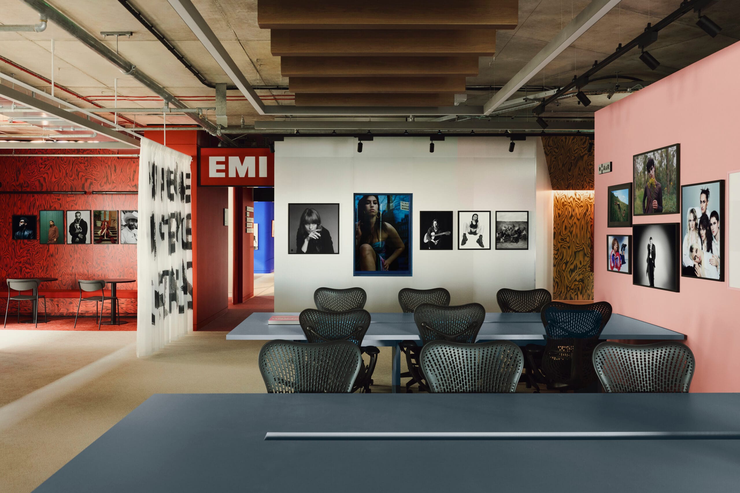 Modern kantoor van Island Records en EMI met blauwe bureaus, roze en rode wanden vol artiestenfoto's en een EMI-bord