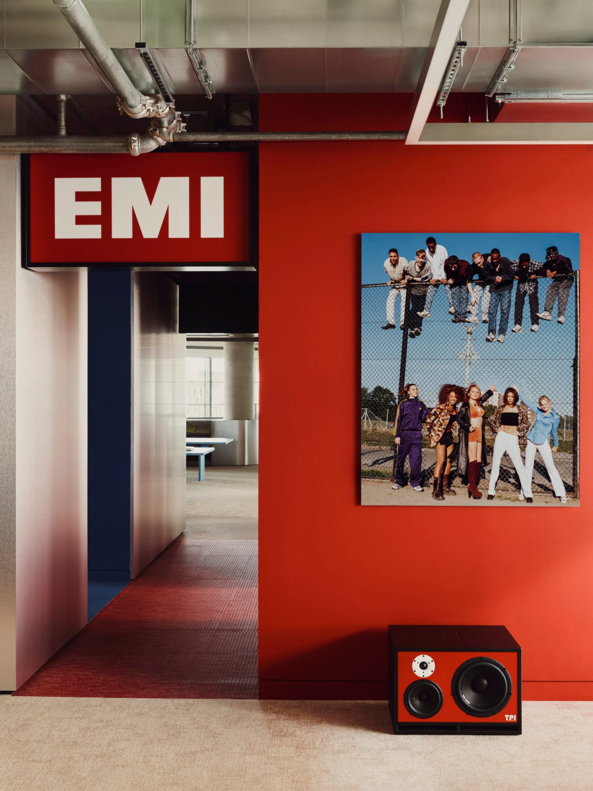 Interieur van het EMI-kantoor met een rode wand, een verlicht EMI-bord en een grote foto van de Spice Girls en een boyband