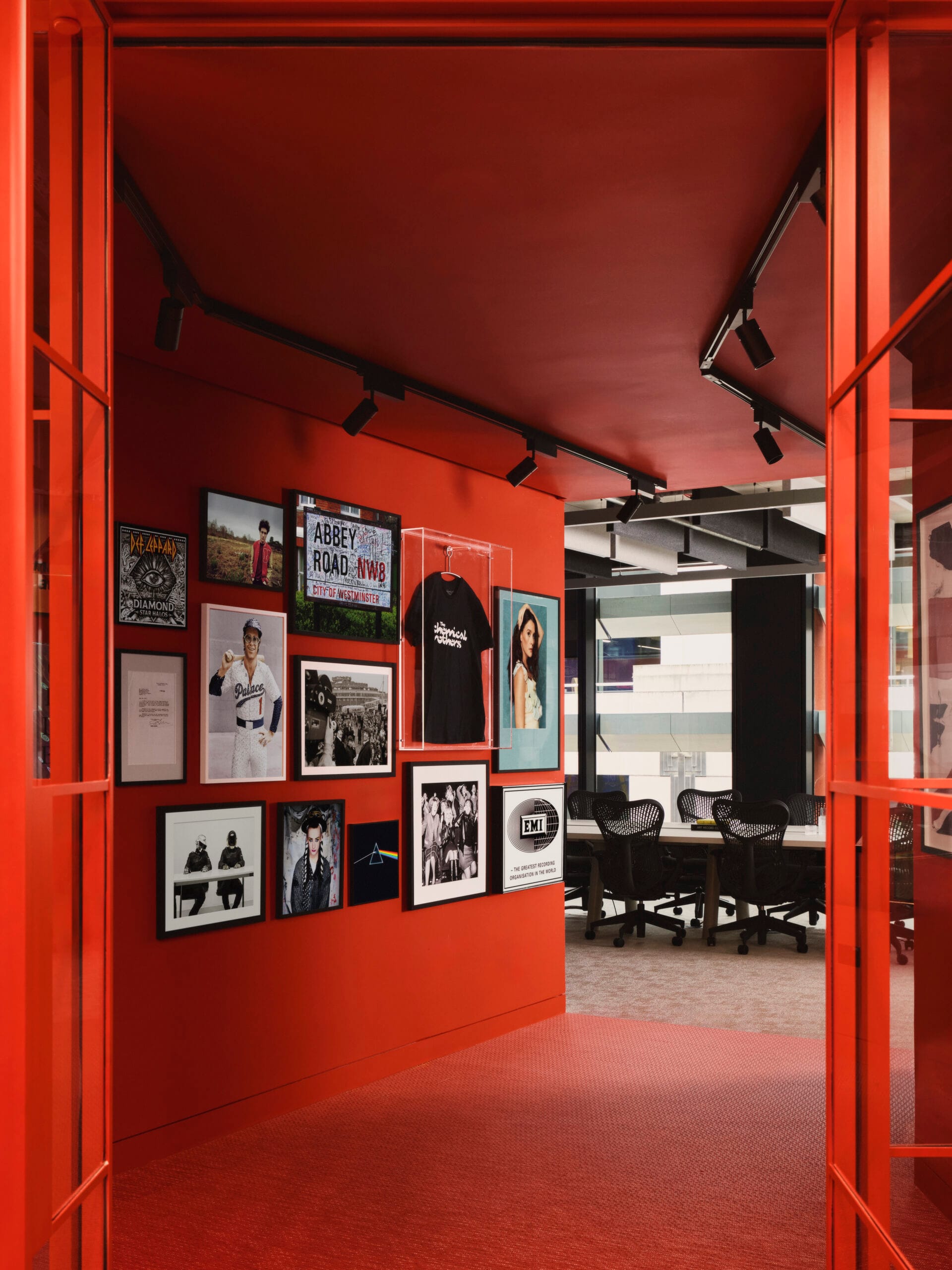 Een felrode gang in het EMI-kantoor met een wand vol ingelijste muziekmemorabilia, foto's en een T-shirt