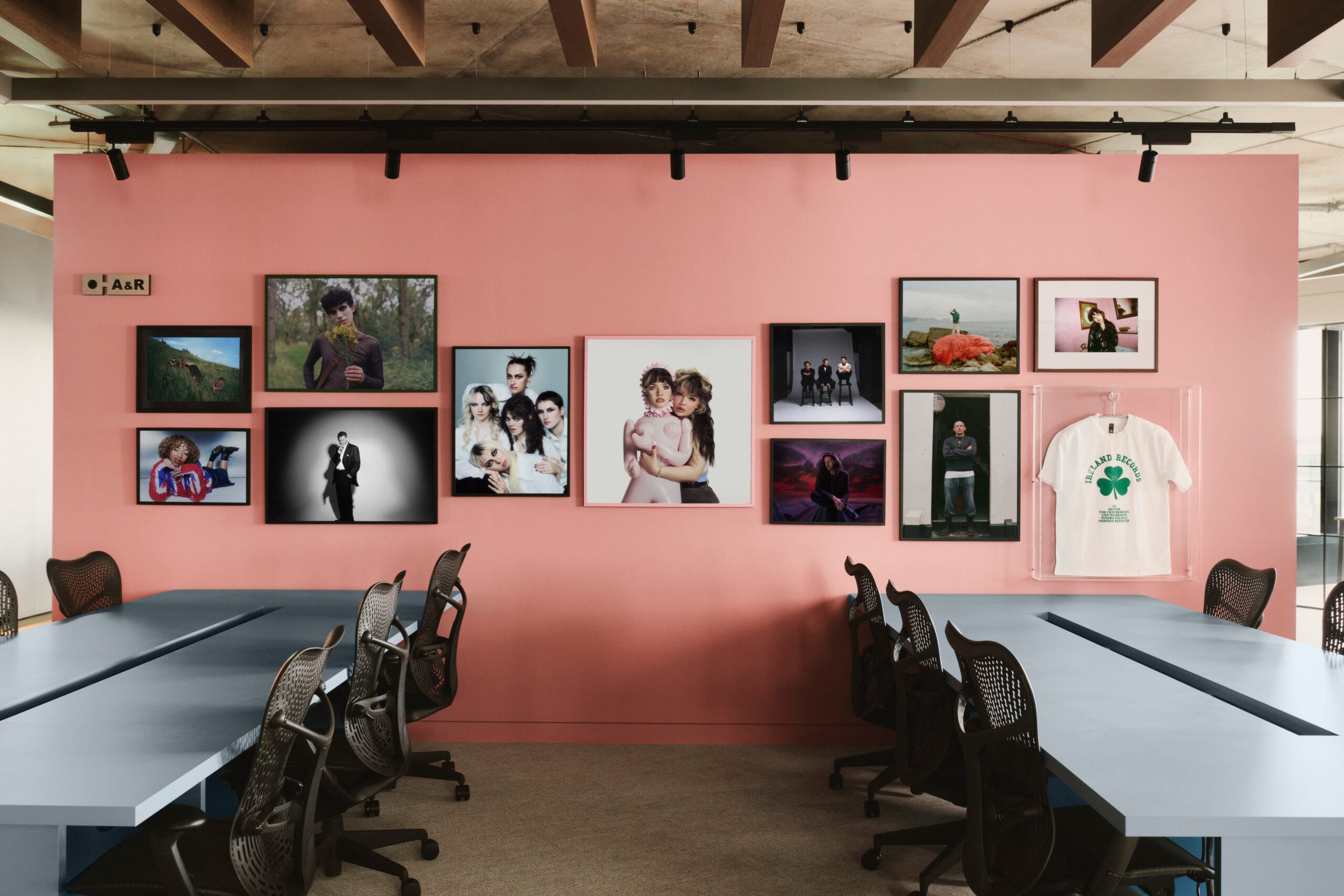 Een roze wand in het Island Records kantoor met diverse ingelijste artiestenfoto's en een wit T-shirt in een vitrine