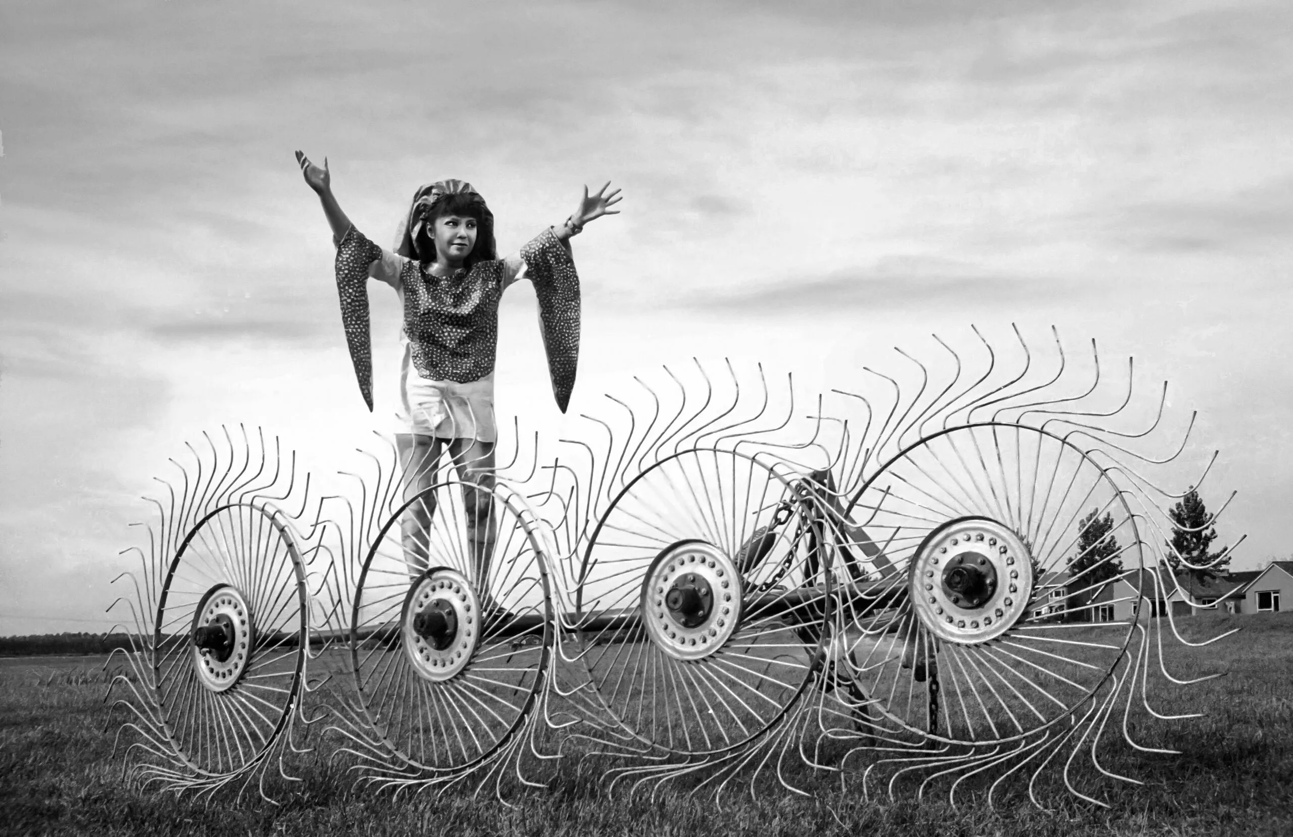 Een jonge Yayoi Kusama in een glanzend kostuum staat met opgeheven armen achter een grote cirkelvormige landbouwmachine in een veld, in Nederland, 1971