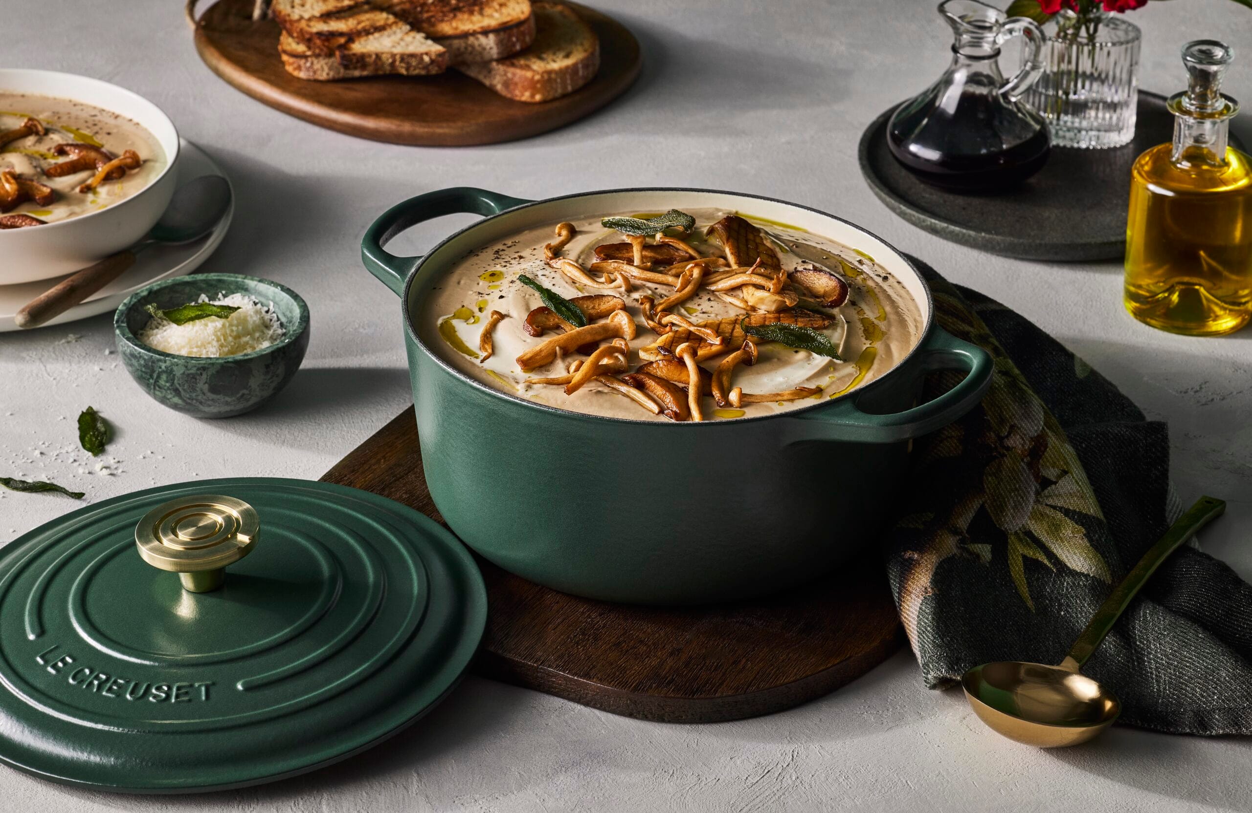 Groene gietijzeren Le Creuset-pan in de kleur Foret gevuld met romige paddenstoelensoep, gegarneerd met gebakken paddenstoelen en salie