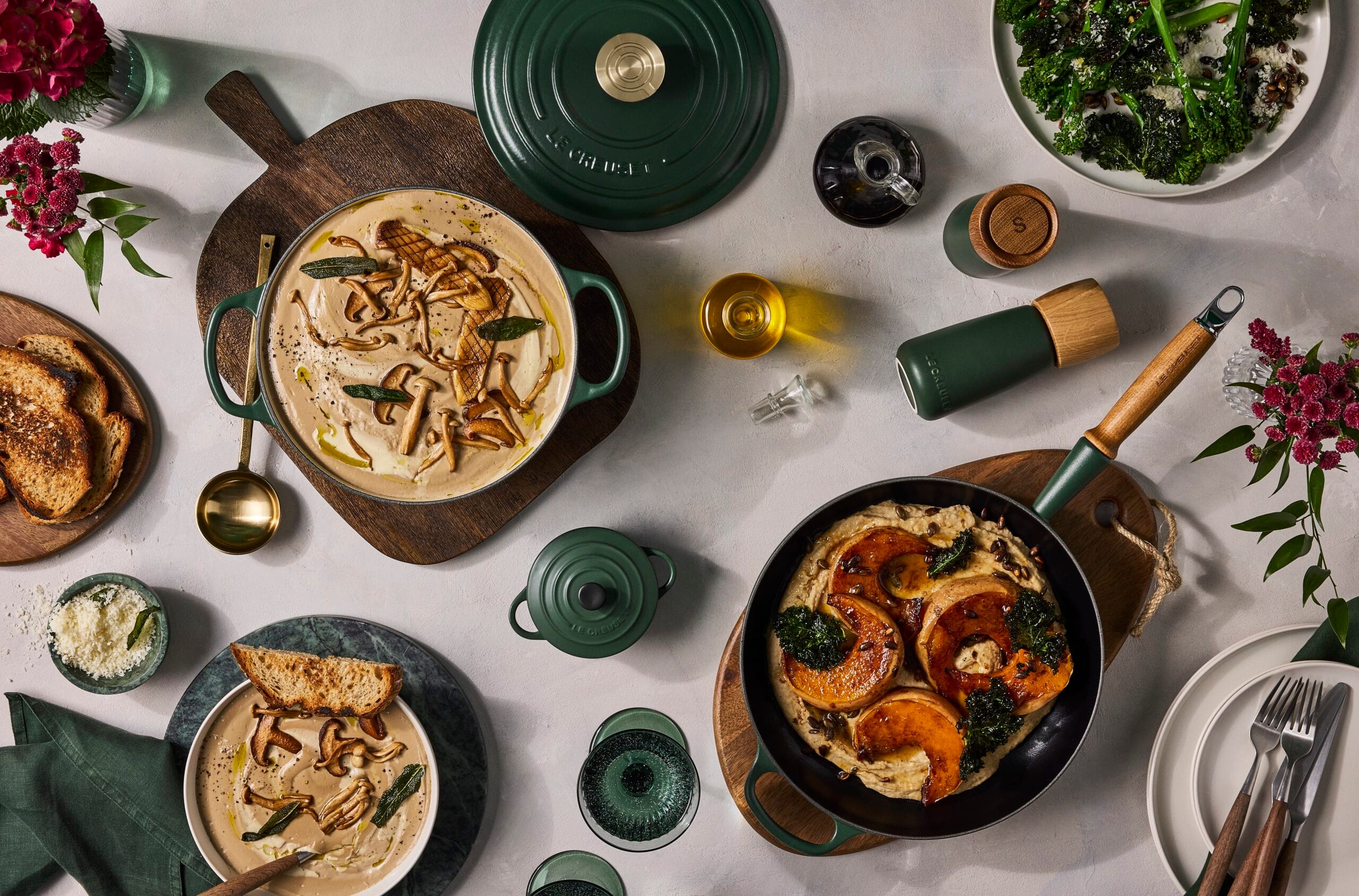 Gedekte tafel met donkergroene pannen van Le Creuset in de nieuwe kleur Fôret, gevuld met paddenstoelensoep en geroosterde pompoen