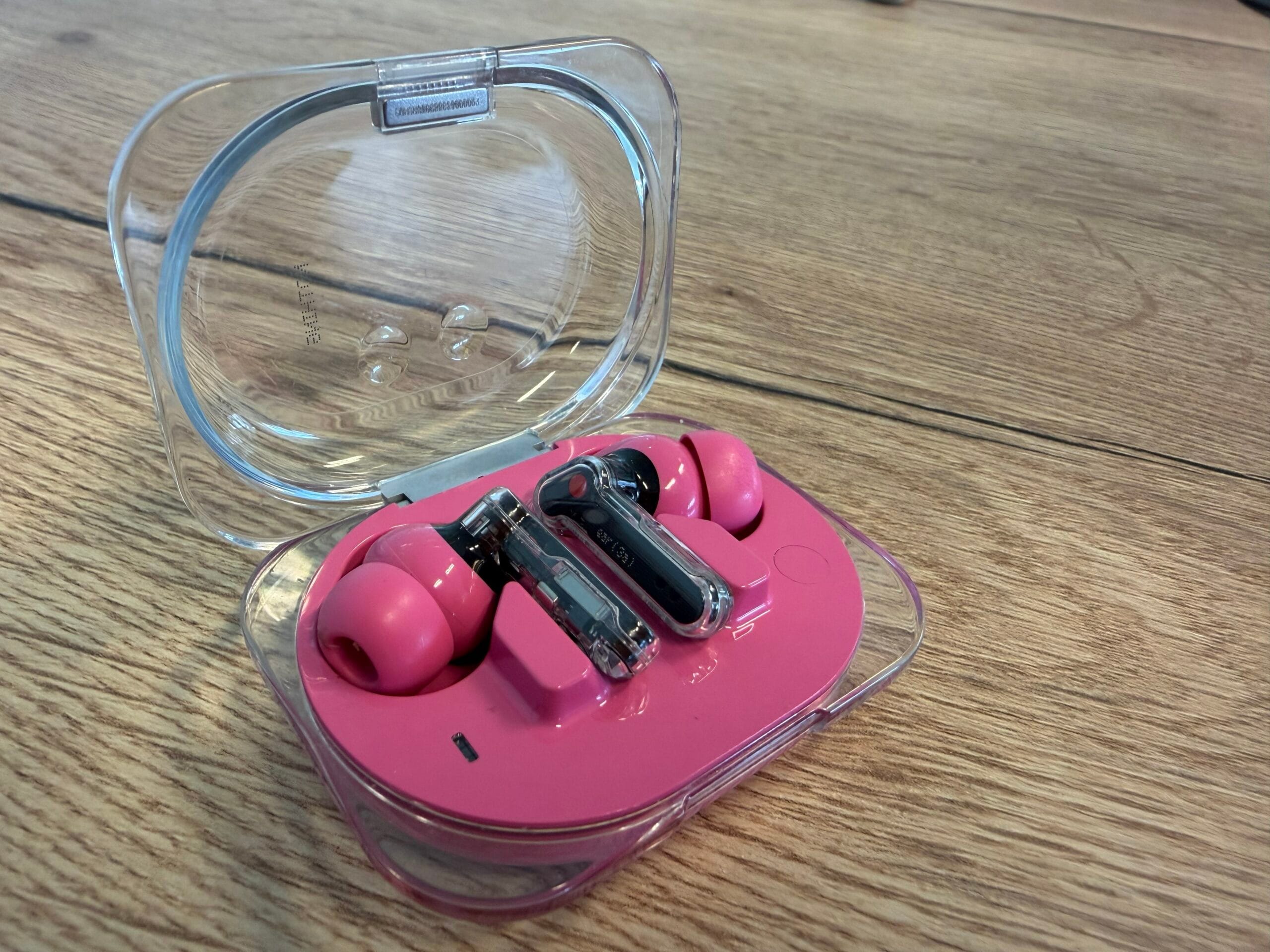 Roze Nothing Ear (3a) oordopjes in een open, transparante oplaadcase op een houten ondergrond