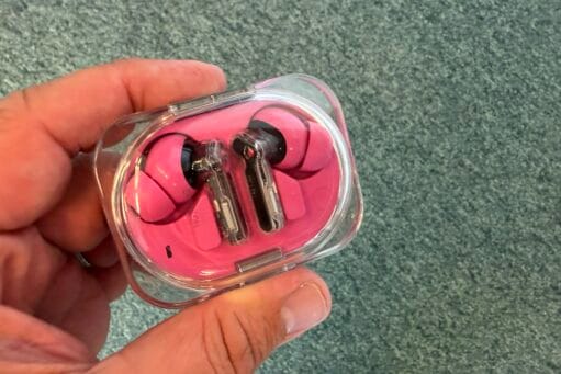 Roze draadloze oordopjes met transparante pootjes in een doorzichtig oplaaddoosje, vastgehouden in een hand